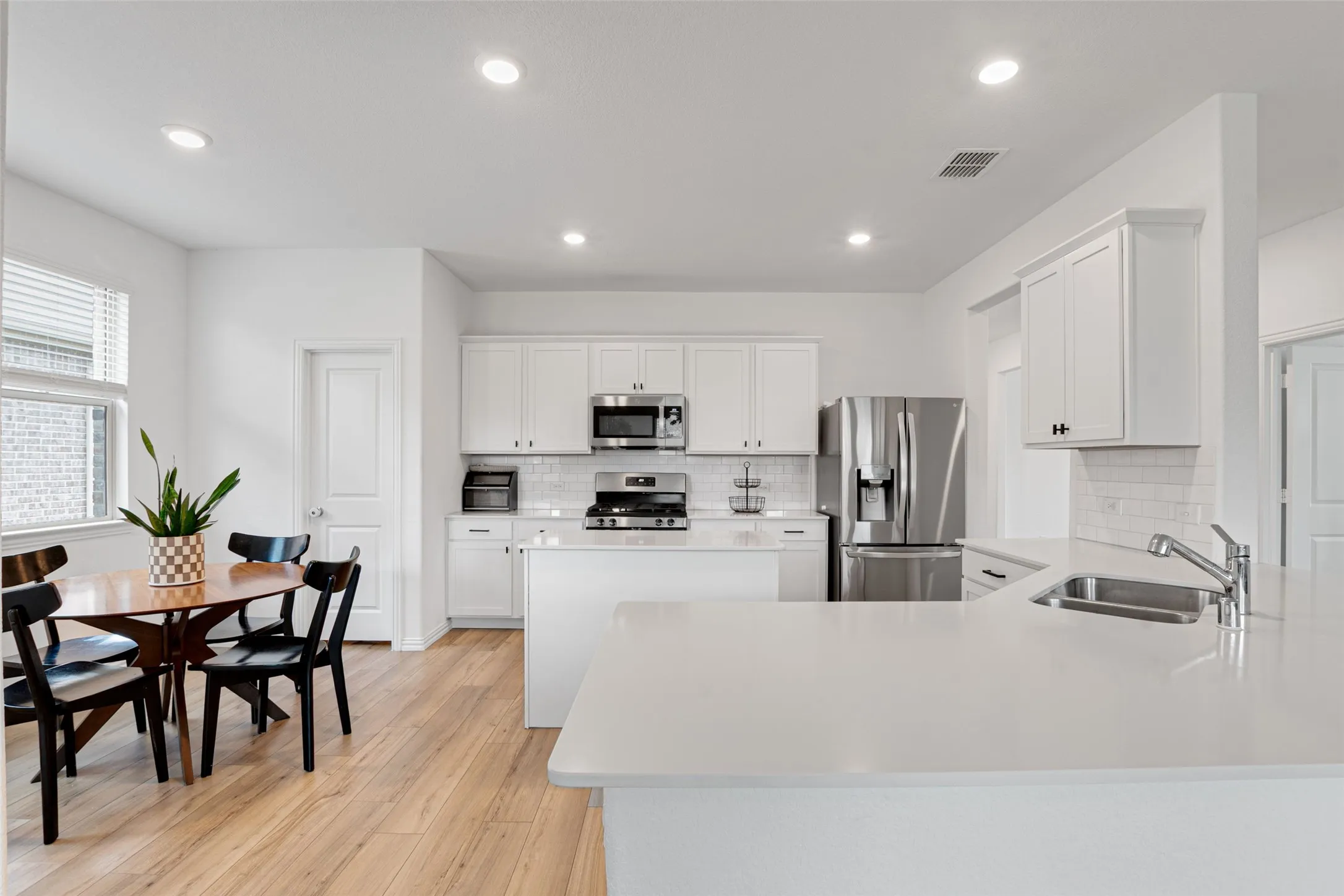 Open-concept kitchen and dining area featuring LVP flooring, white cabinetry, stainless steel appliances, and a subway tile backsplash