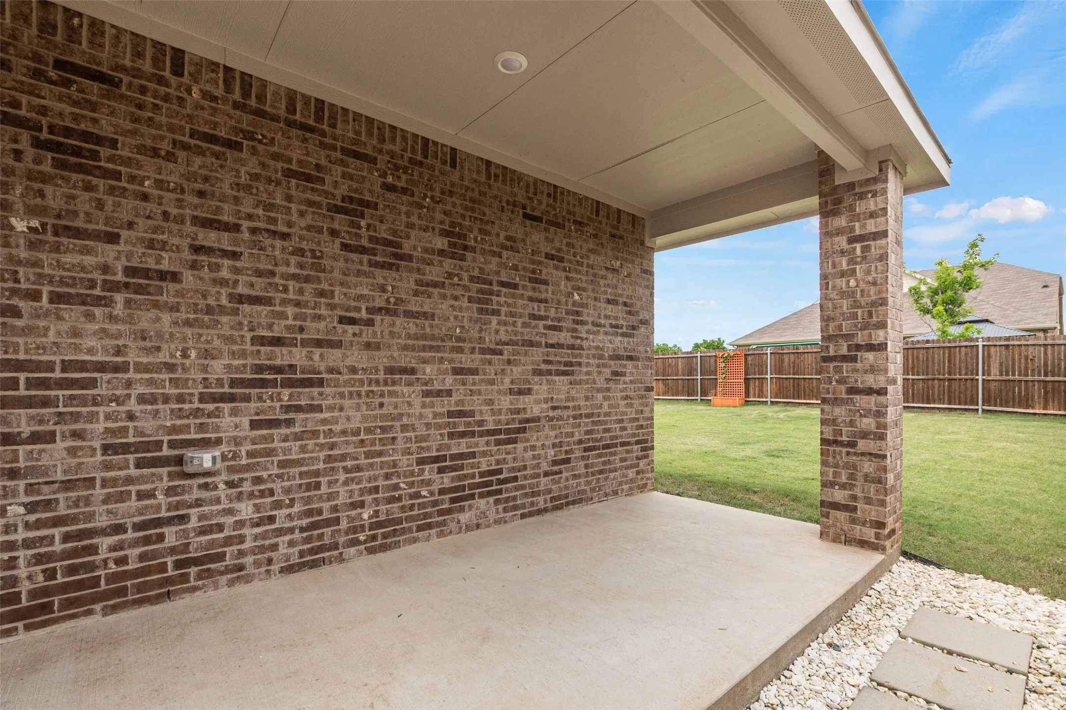Covered concrete patio featuring a recessed light, brick column, and a full brick exterior wall