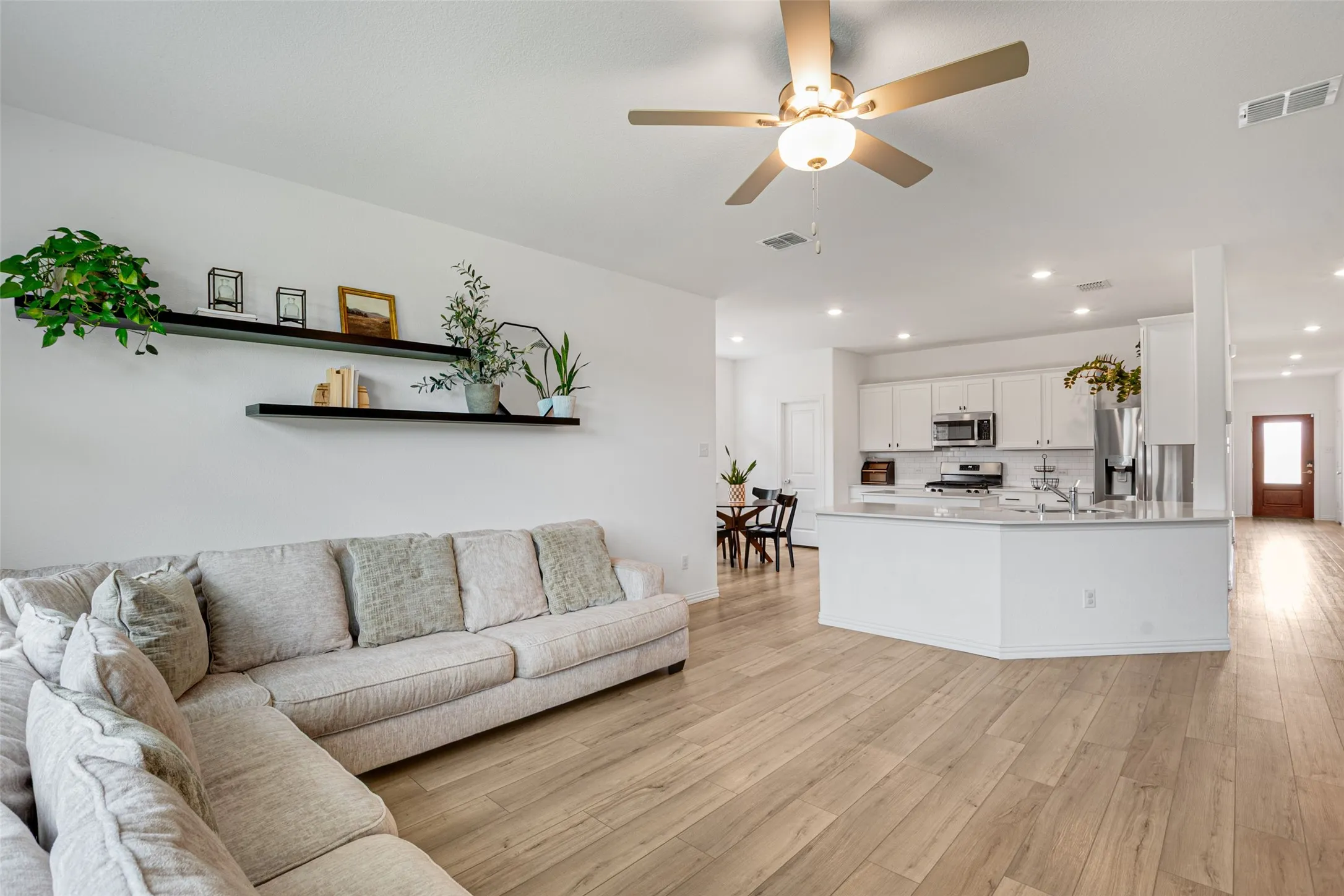 Open-concept living space featuring LVP  flooring, a kitchen island with stone countertop, white shaker cabinetry, recessed lighting, and a ceiling fan