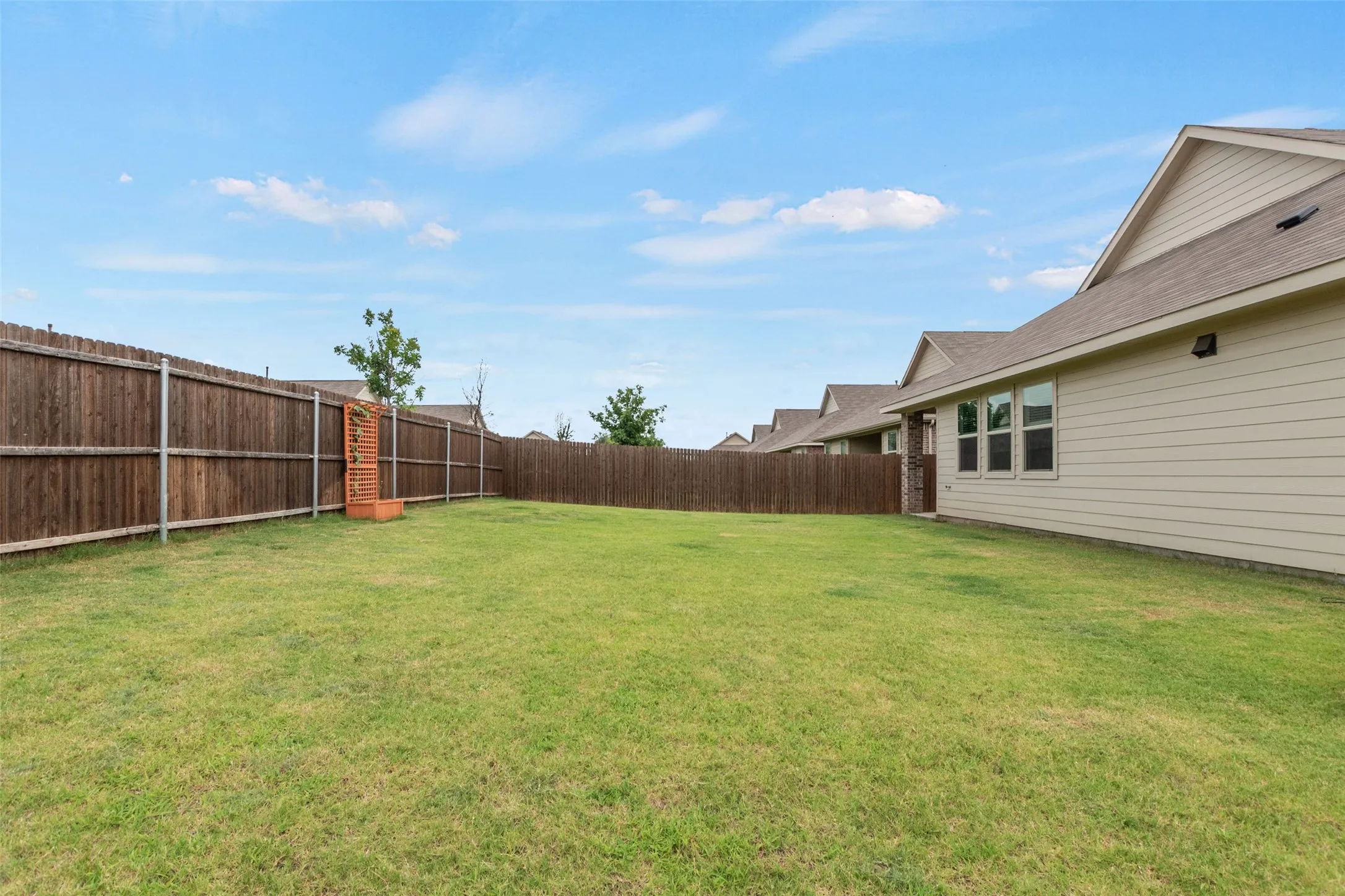 Expansive fenced backyard featuring a verdant lawn, perimeter wood fencing, and a neutral-toned exterior siding