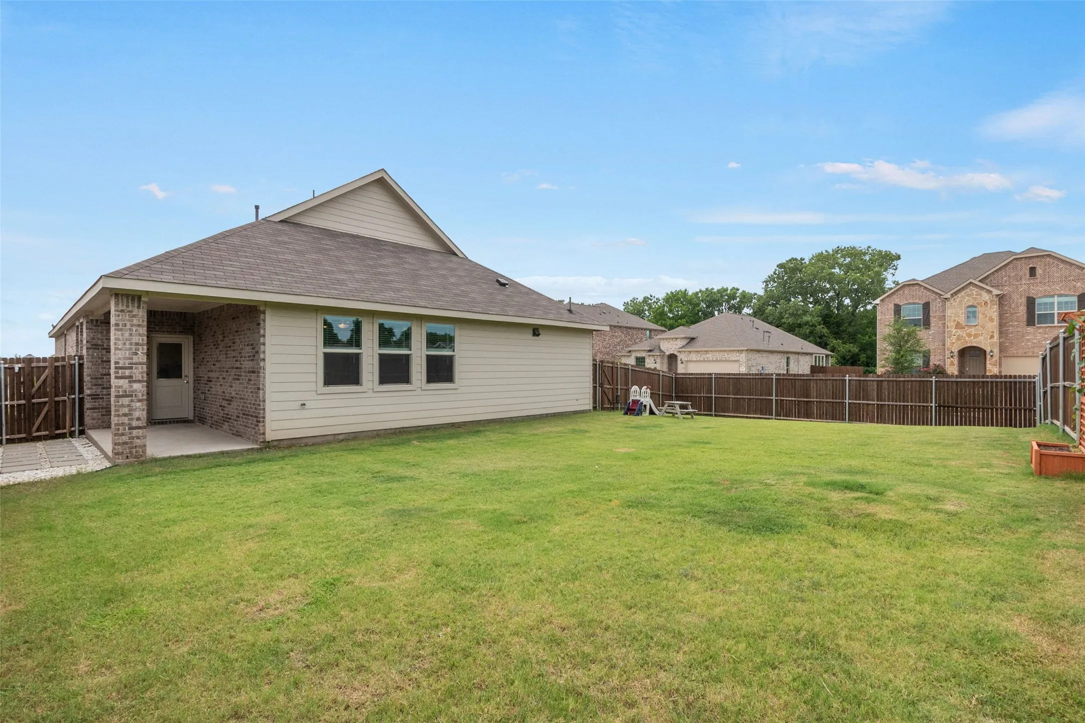 Expansive backyard featuring a covered patio with brick columns, a wood privacy fence, and a generous lawn space