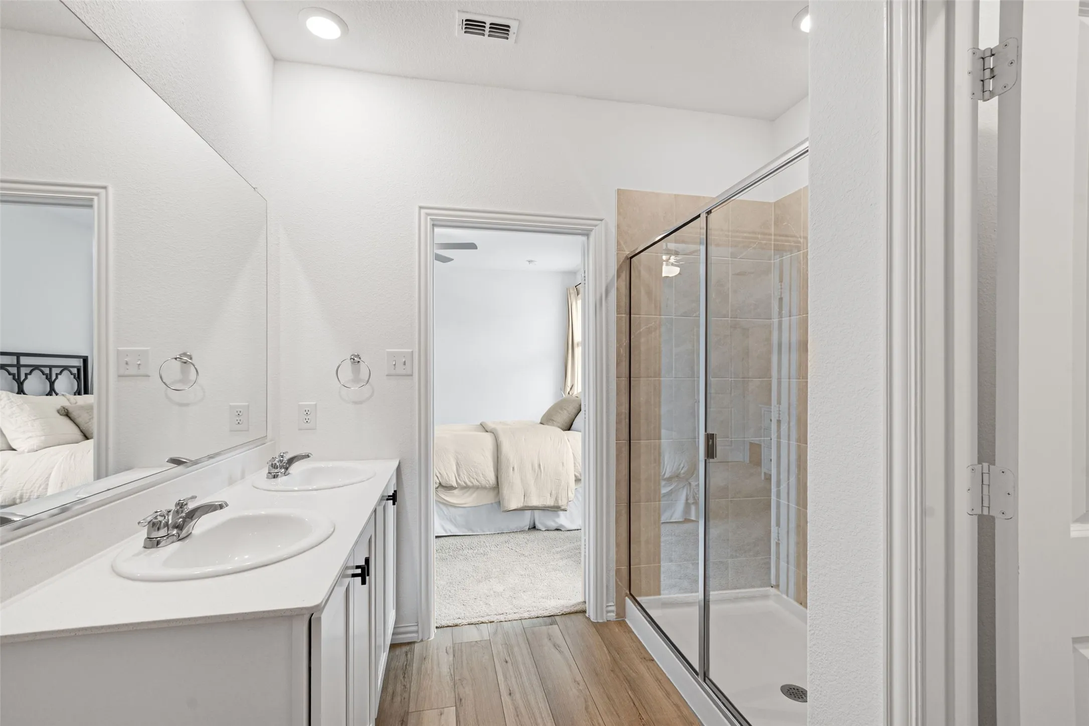 Bathroom featuring a double vanity with white cabinetry, a large mirrored wall, and LVP  flooring