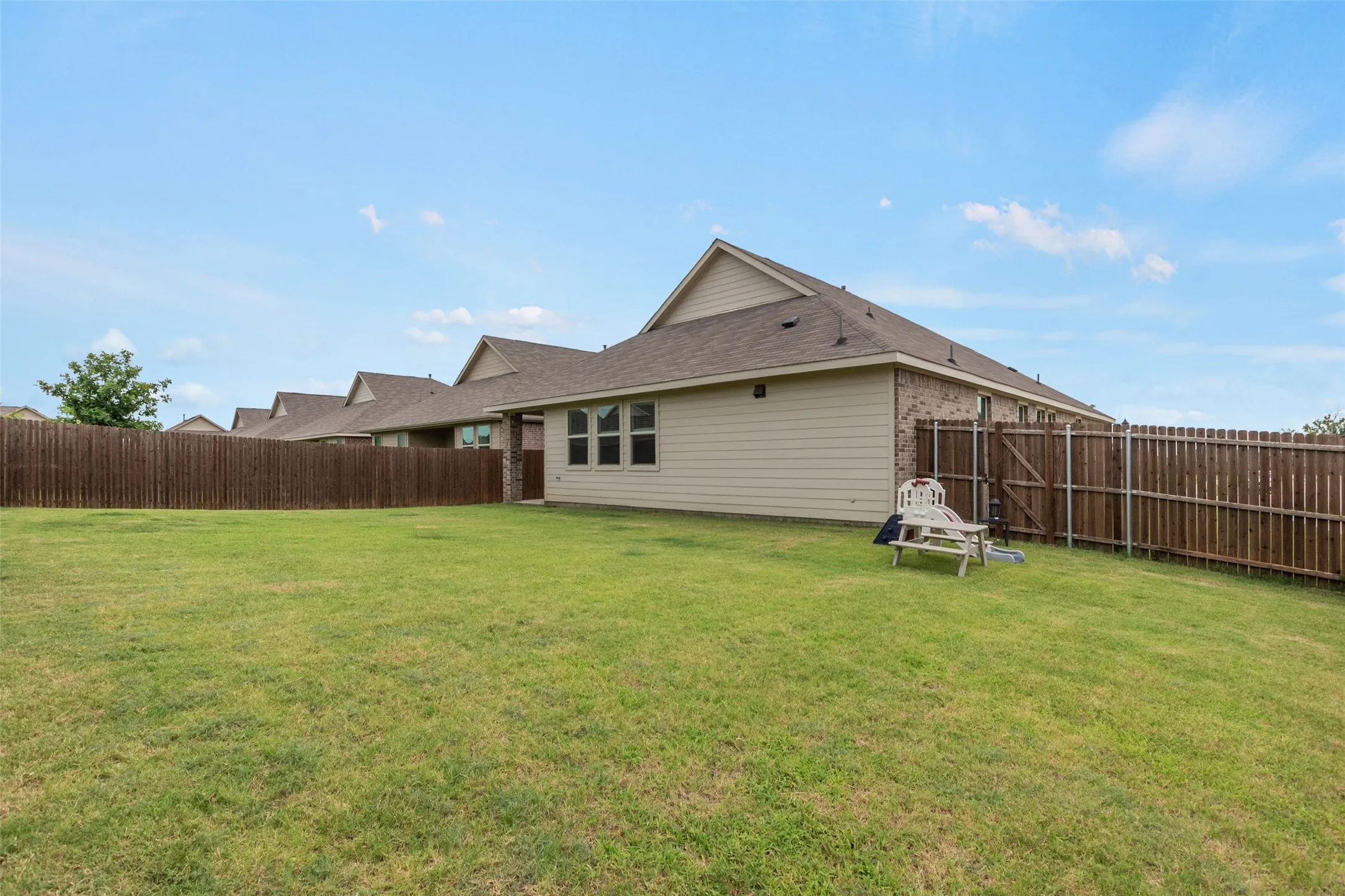 Spacious grassy yard featuring a wood privacy fence and a tan siding exterior