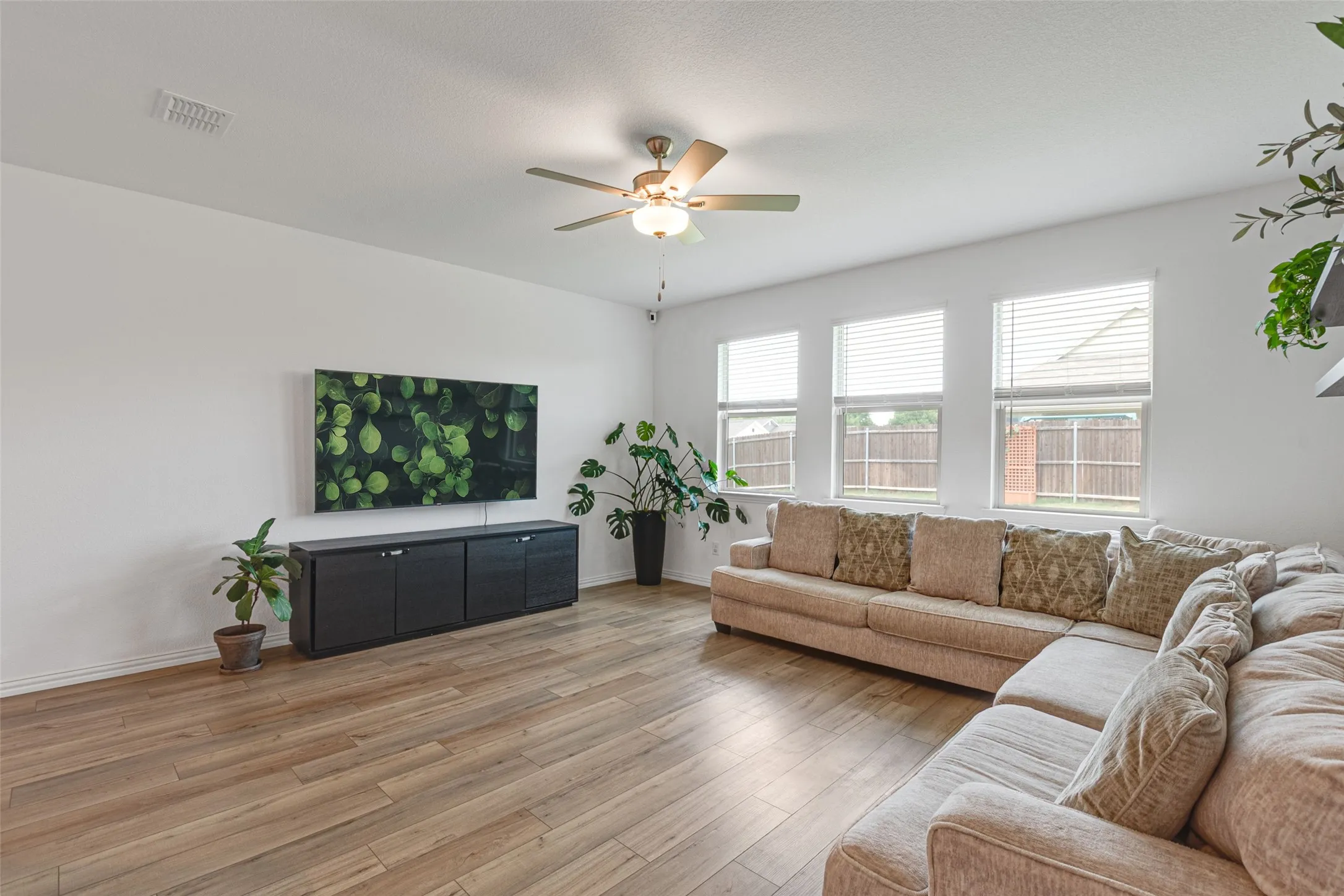 Spacious living area featuring LVPflooring, ample natural light from multiple windows, and a ceiling fan with integrated lighting