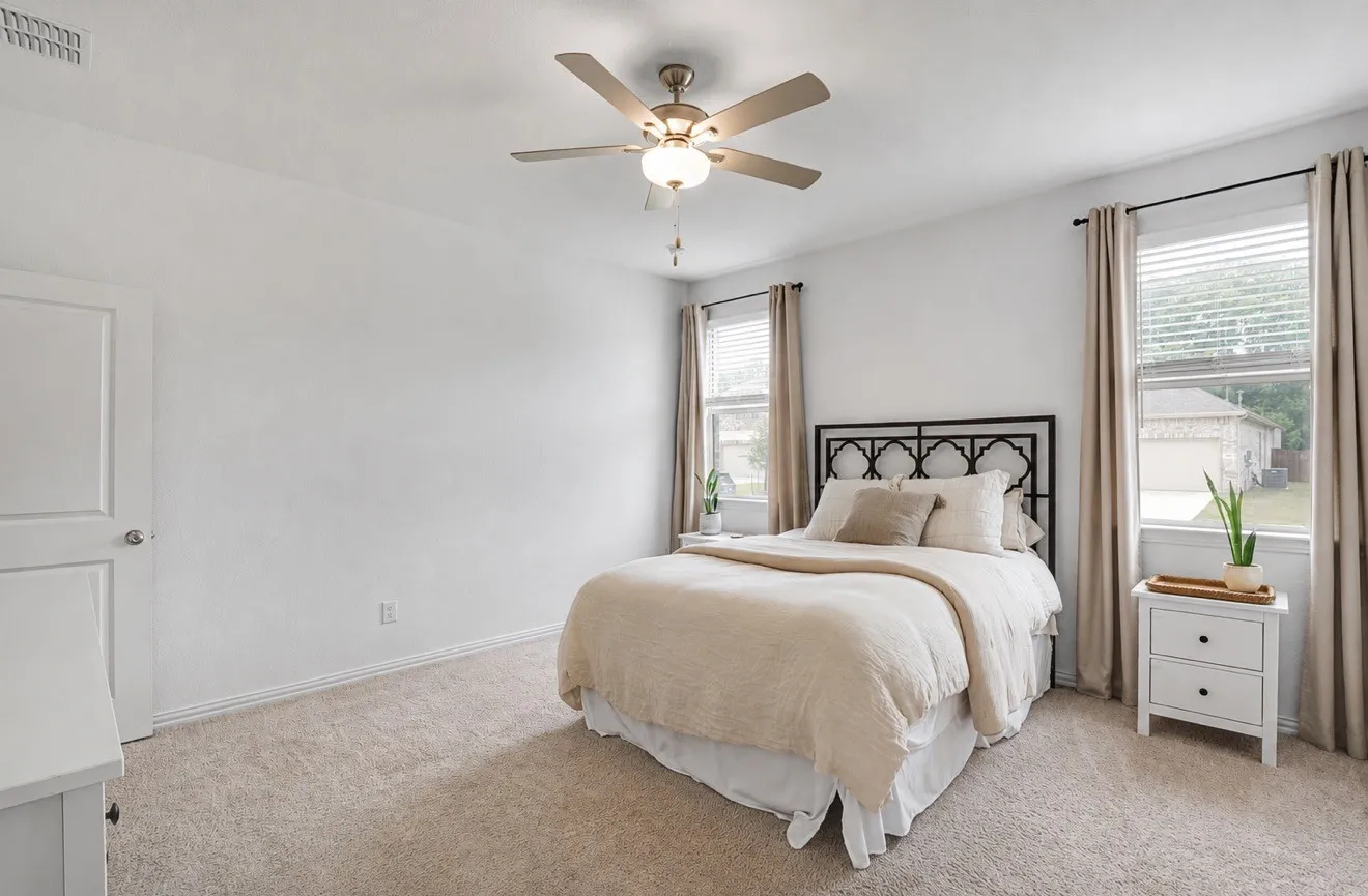 Carpeted room featuring a ceiling fan with integrated lighting, multiple windows with blinds and drapes, and a white paneled door