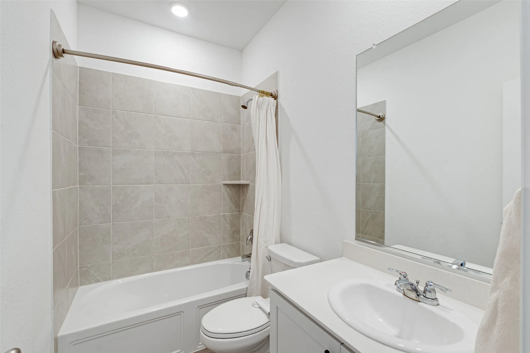 Bathroom featuring a white bathtub, ceramic tile surround, recessed shower niche, single vanity with an oval sink, and a large wall mirror
