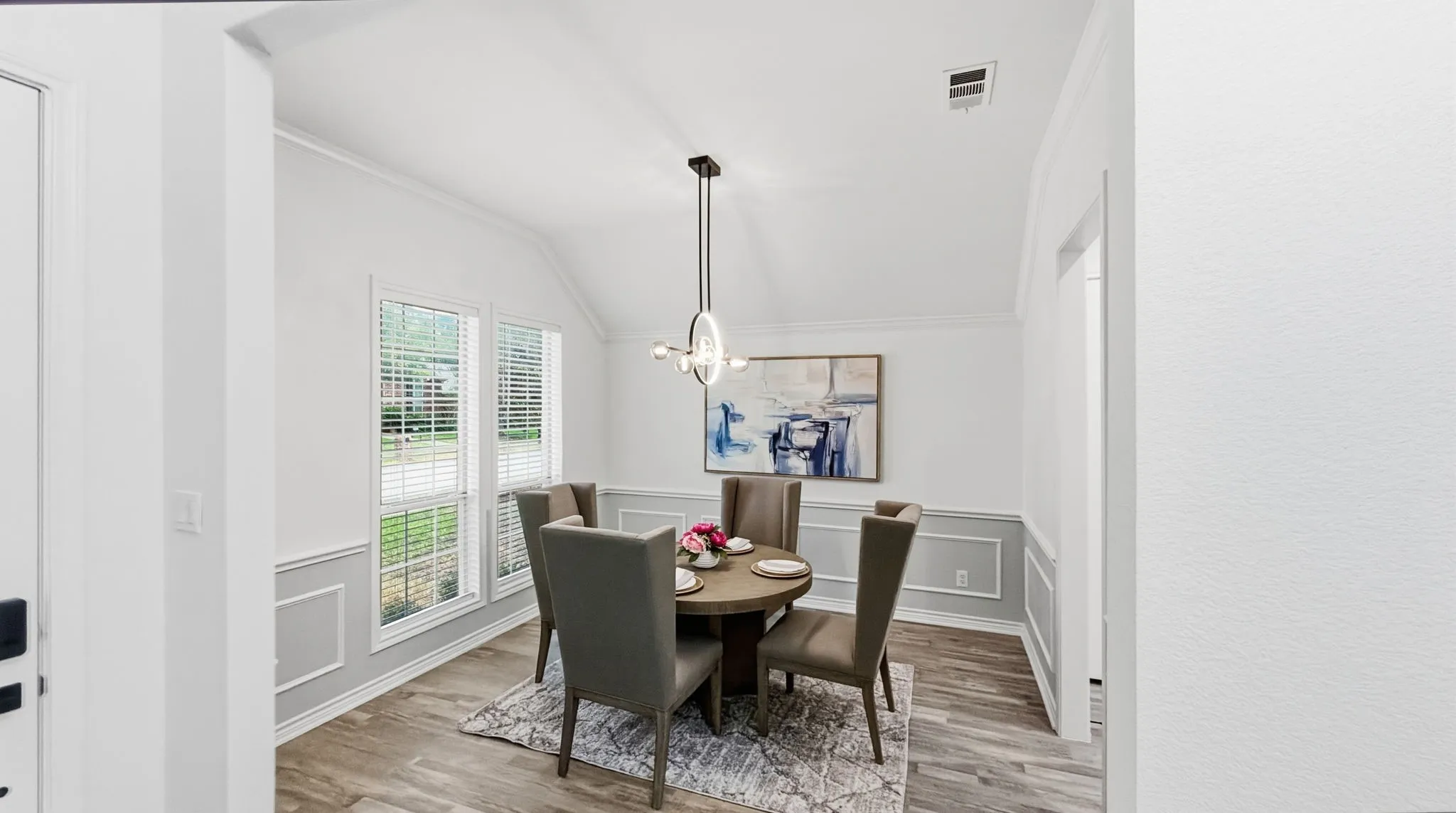 Vaulted ceiling with crown molding, wood-finish flooring, wainscoting, contemporary chandelier, and window blinds