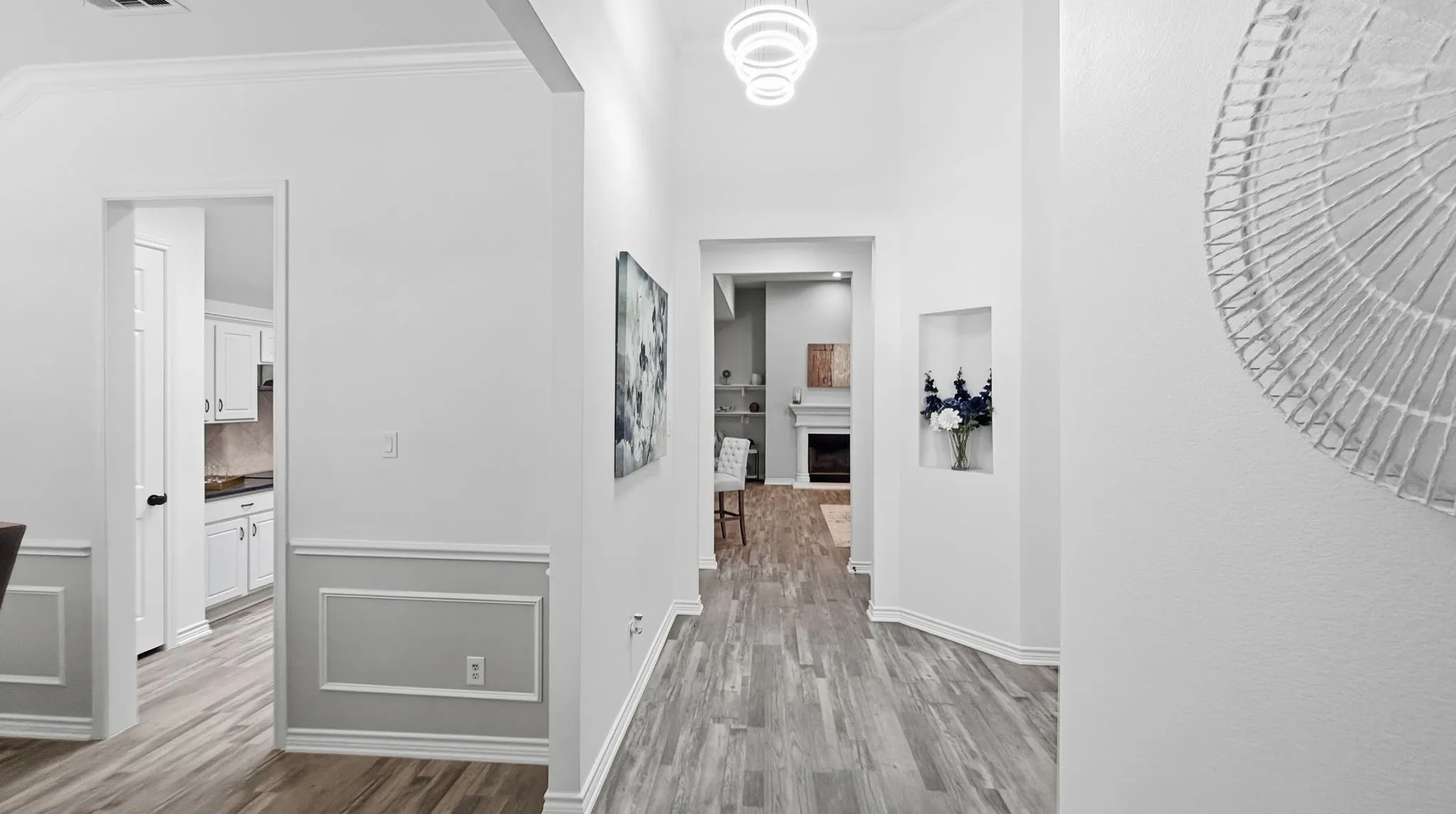 Wood-finish flooring throughout, crown molding, modern chandelier, recessed wall niche, and wainscoting