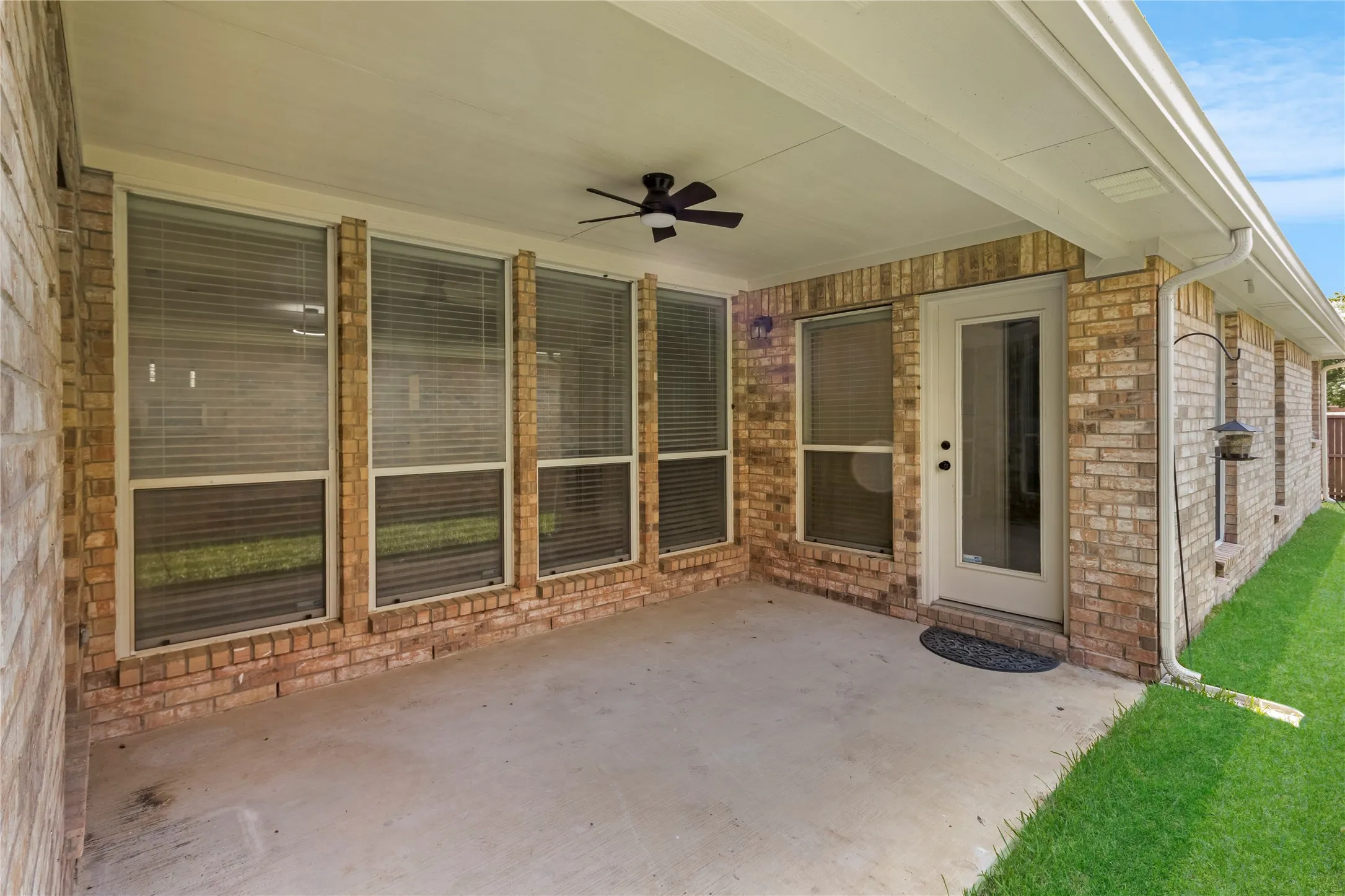 Covered outdoor patio featuring a concrete surface, brick exterior, and a ceiling fan