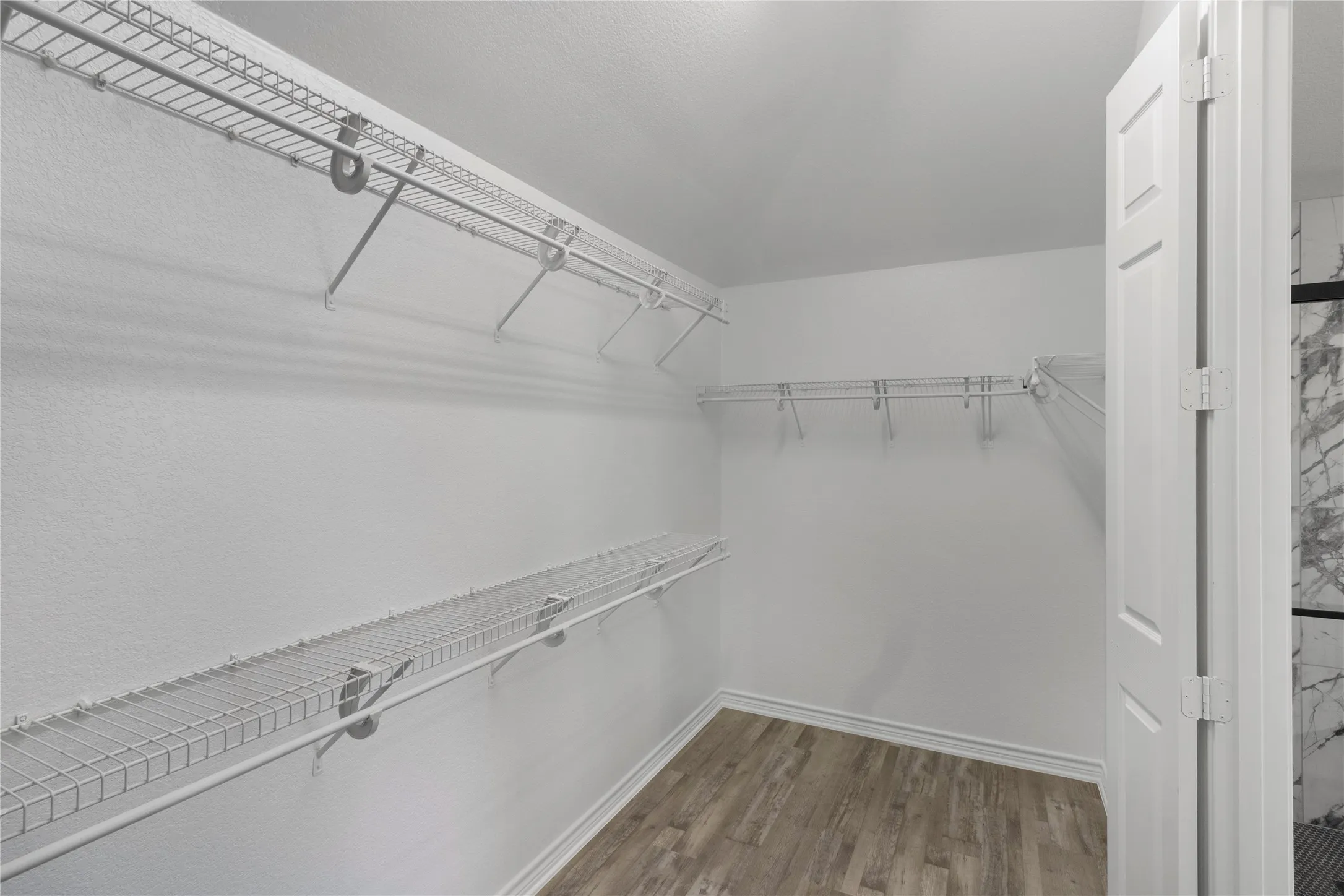 Expansive closet featuring multiple wire shelving units, wood-finish flooring, white baseboards, and a paneled interior door