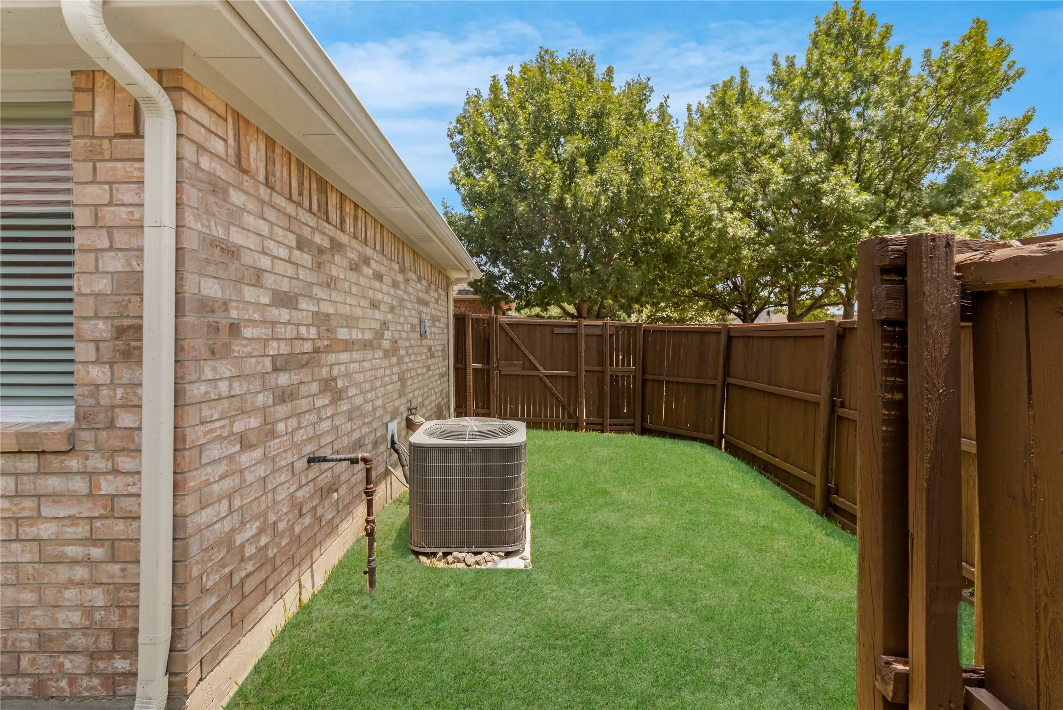 Enclosed side yard featuring a brick exterior wall, mature trees, a wooden privacy fence, and a manicured lawn