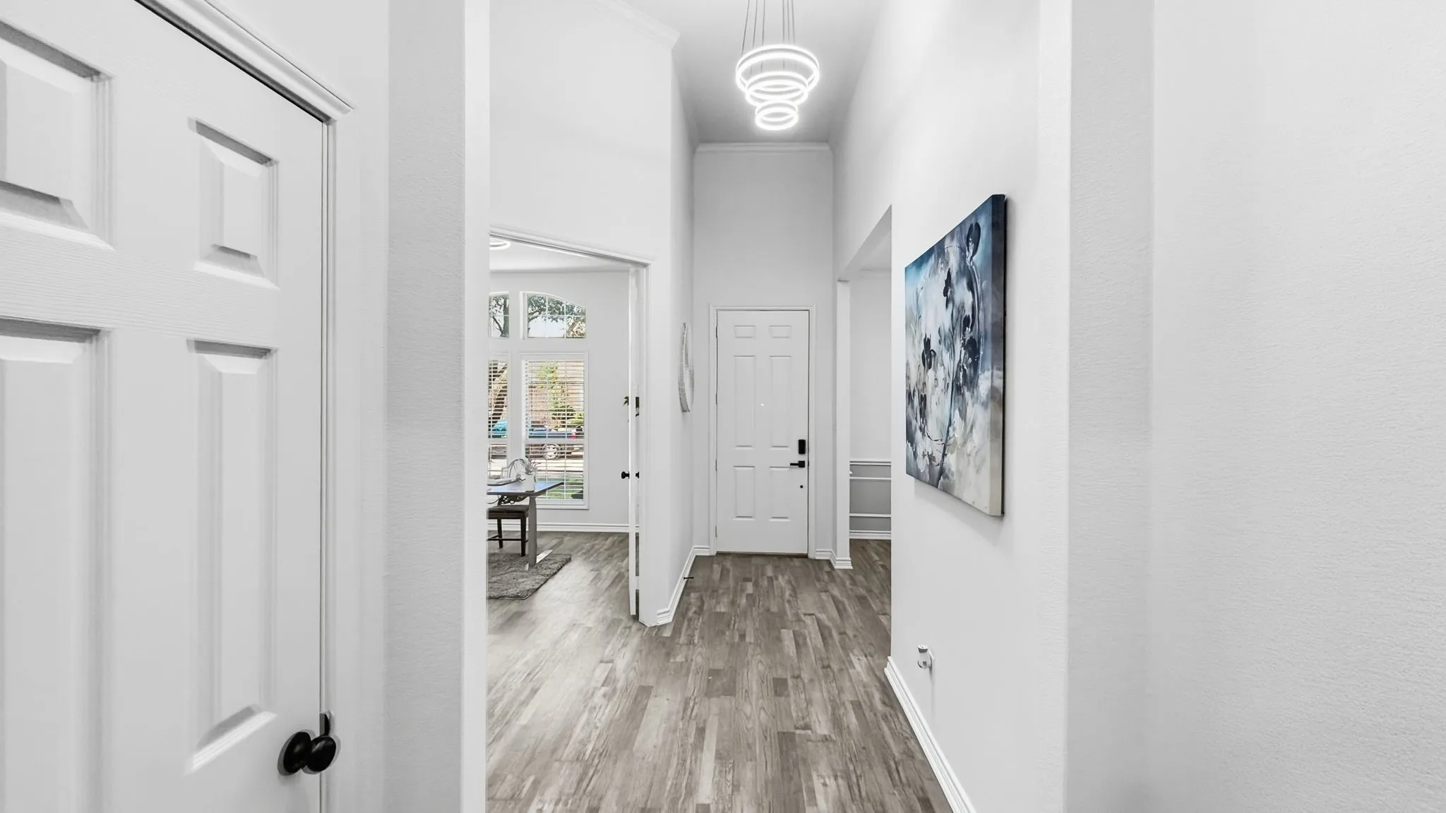 Vaulted ceiling with an attached modern chandelier, wood-finish flooring, and white paneled doors
