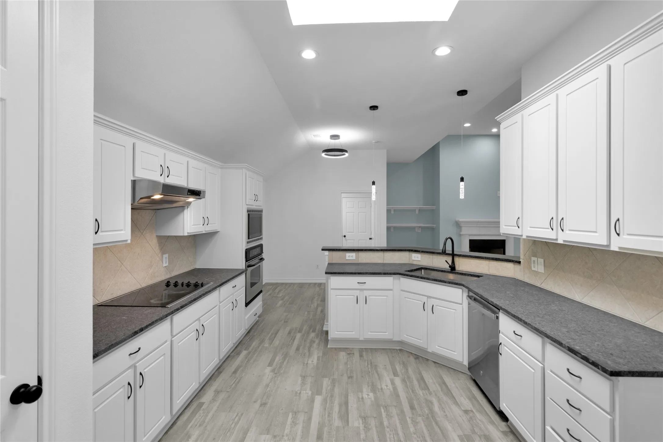 Contemporary kitchen featuring white cabinetry, dark countertops, built-in stainless steel appliances, a skylight, and LVP flooring