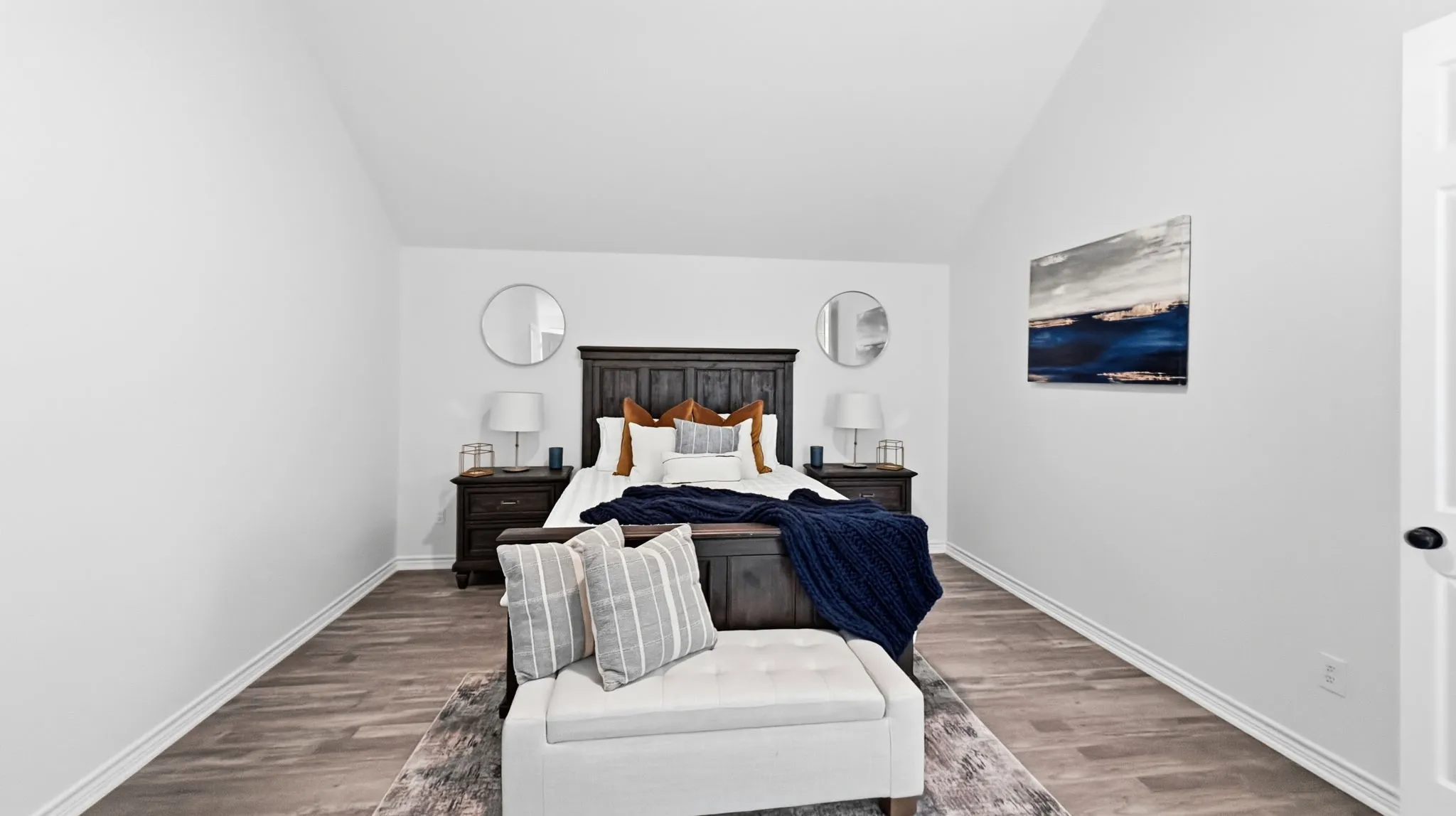 Vaulted ceiling, wood-finish flooring, white walls, and a white door with black hardware
