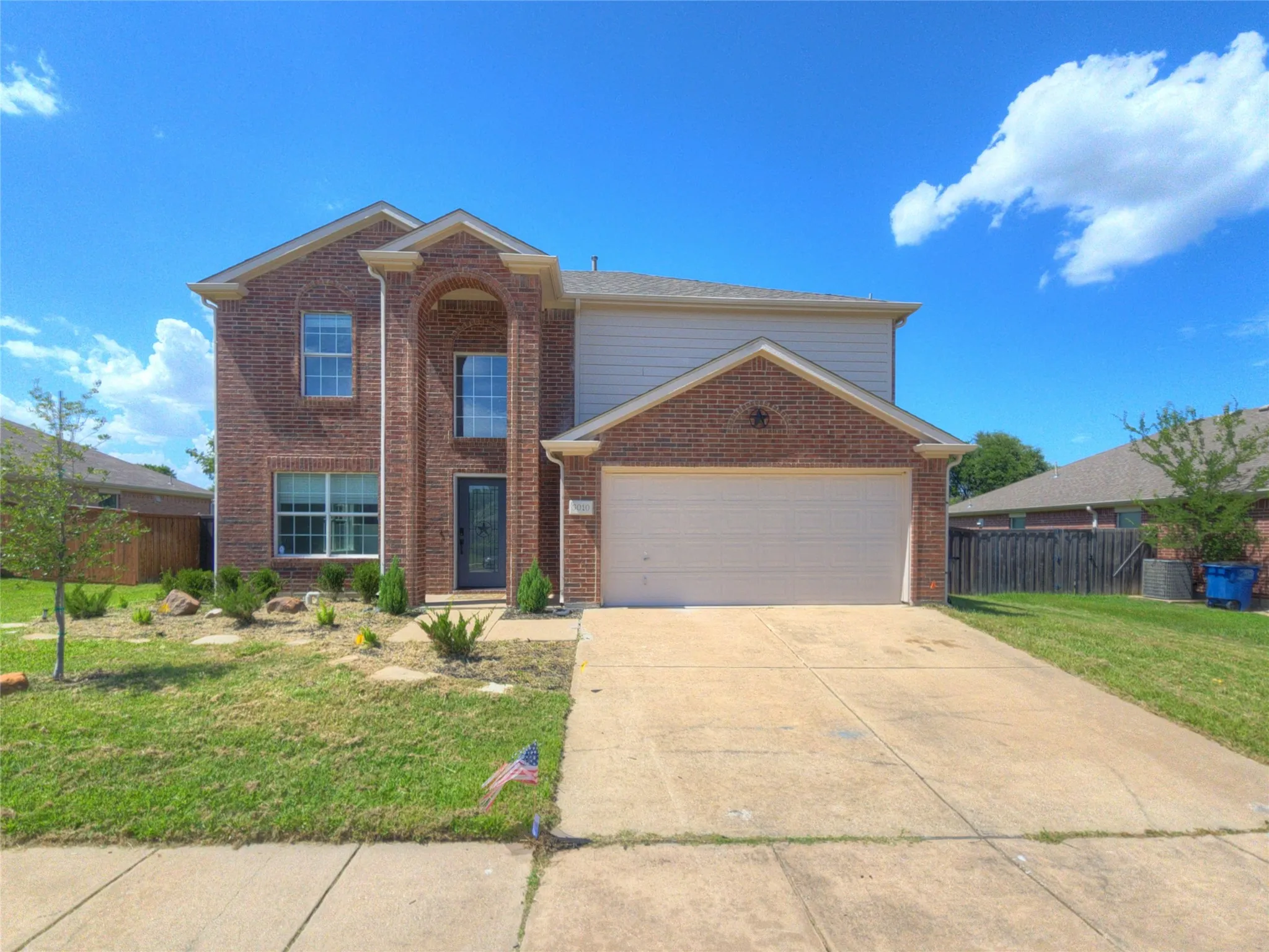 Brick and siding exterior featuring an arched entry, a two-car garage, and a landscaped front yard with stepping stones