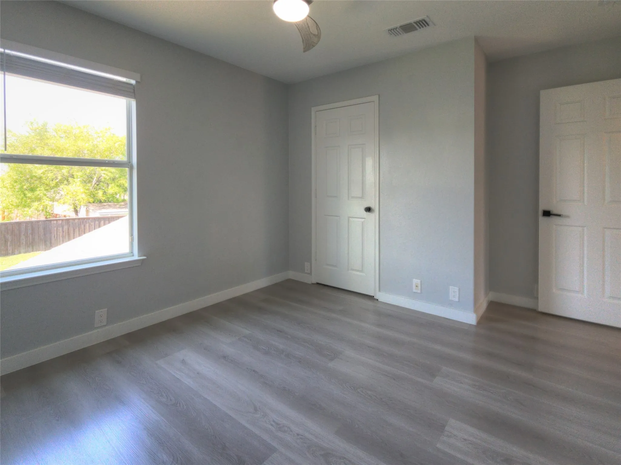 Spacious room with light gray walls, wood-finish flooring, and white trim
