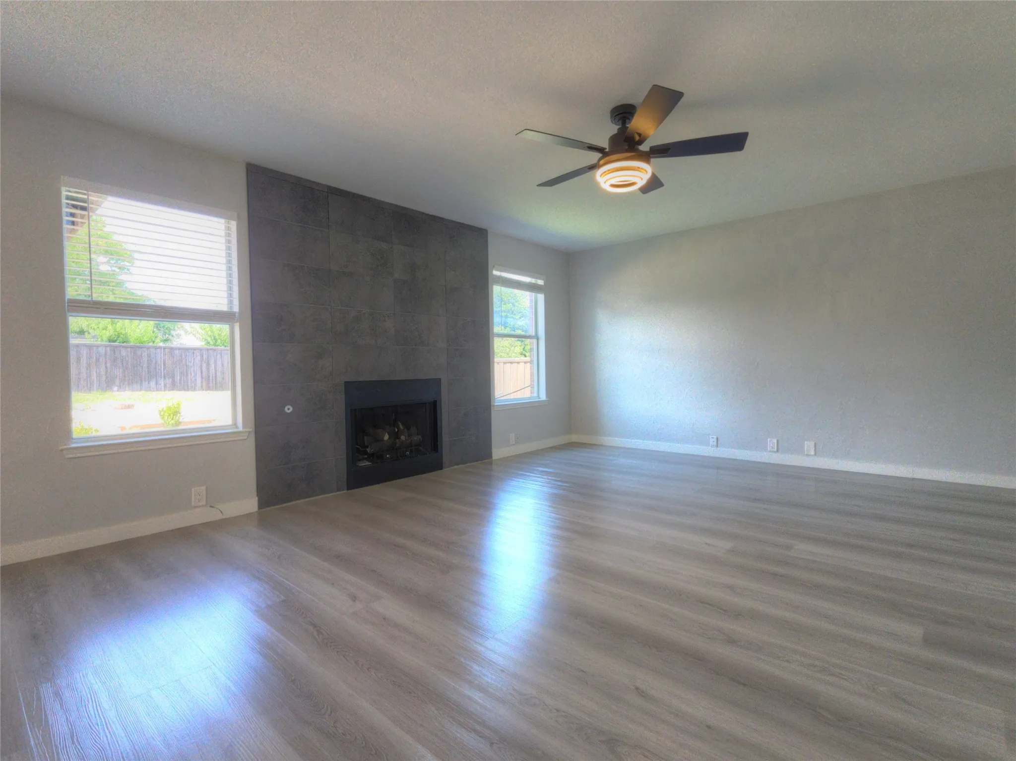 Spacious interior featuring wood-finish flooring, a contemporary fireplace with dark tile surround, and a ceiling fan with integrated lighting