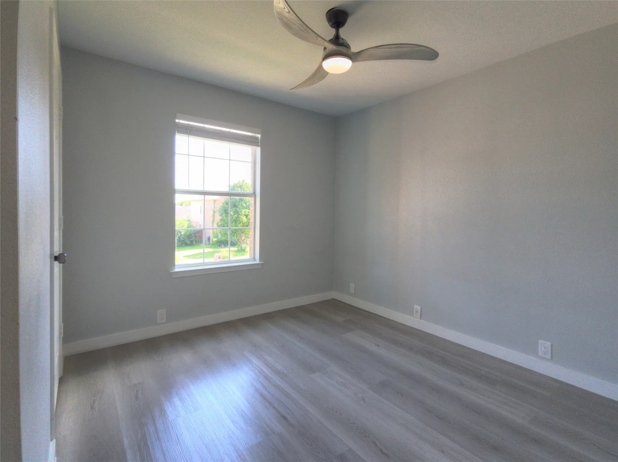 Room featuring wood-finish flooring, a window with horizontal blinds, and a ceiling fan with integrated lighting