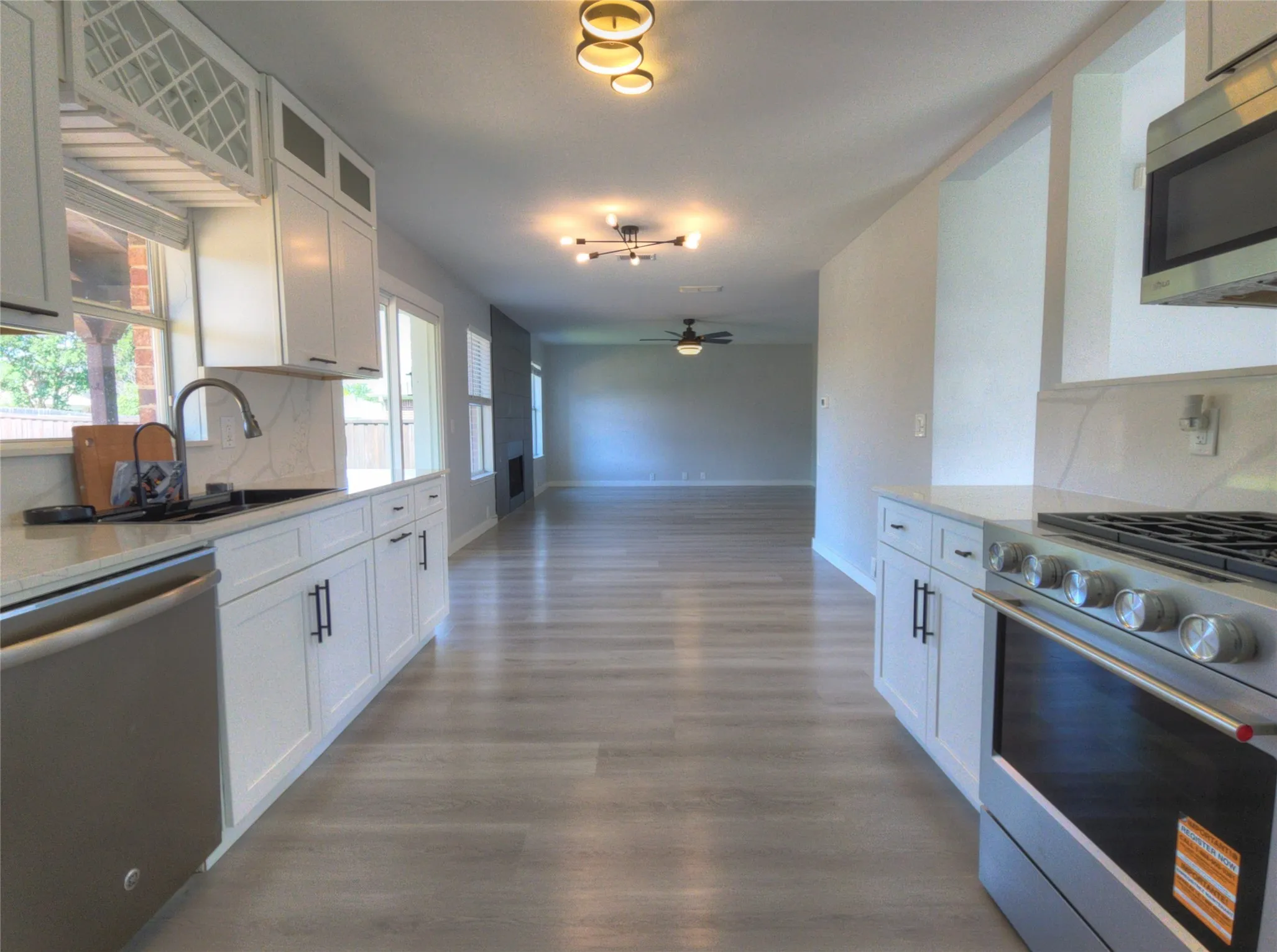 Open-concept kitchen featuring white shaker cabinetry, stainless steel appliances, stone countertops, and wood-finish flooring extending into living areas