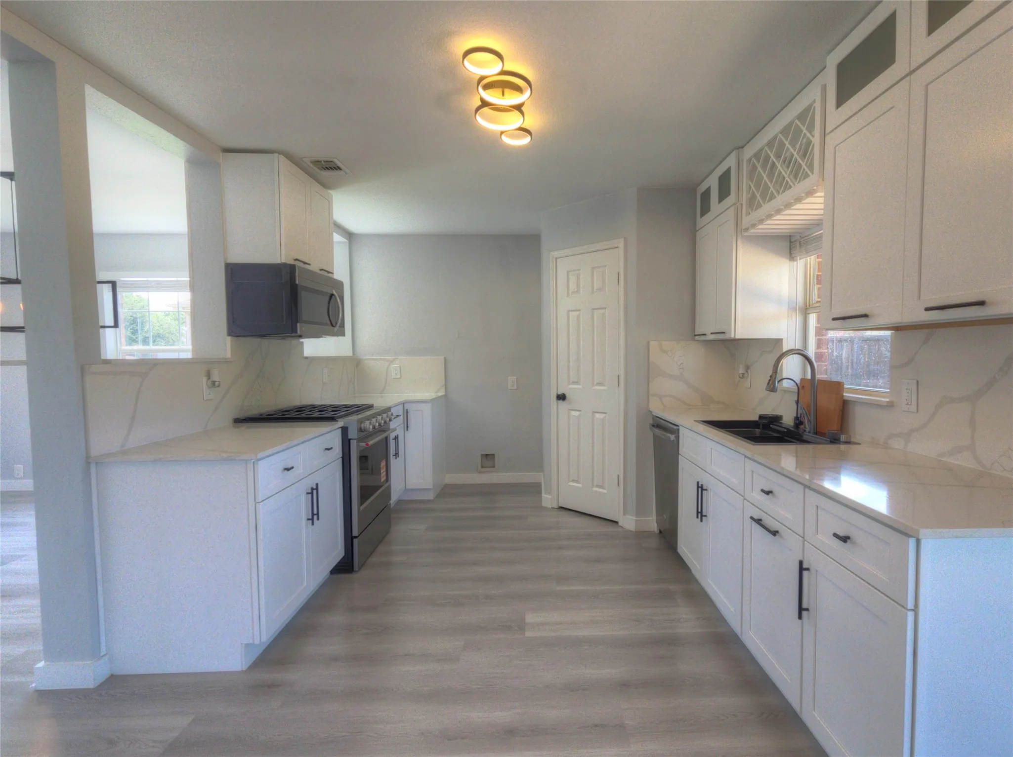 Contemporary kitchen featuring white cabinetry, light-toned wood-finish flooring, and white countertops with a matching backsplash