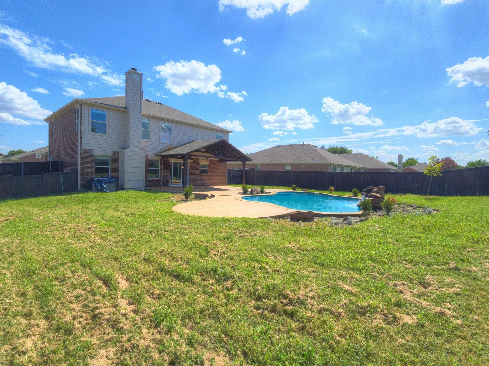 Expansive backyard featuring a gunite swimming pool with rock waterfall, a covered patio with recessed lighting, and a generously sized lawn