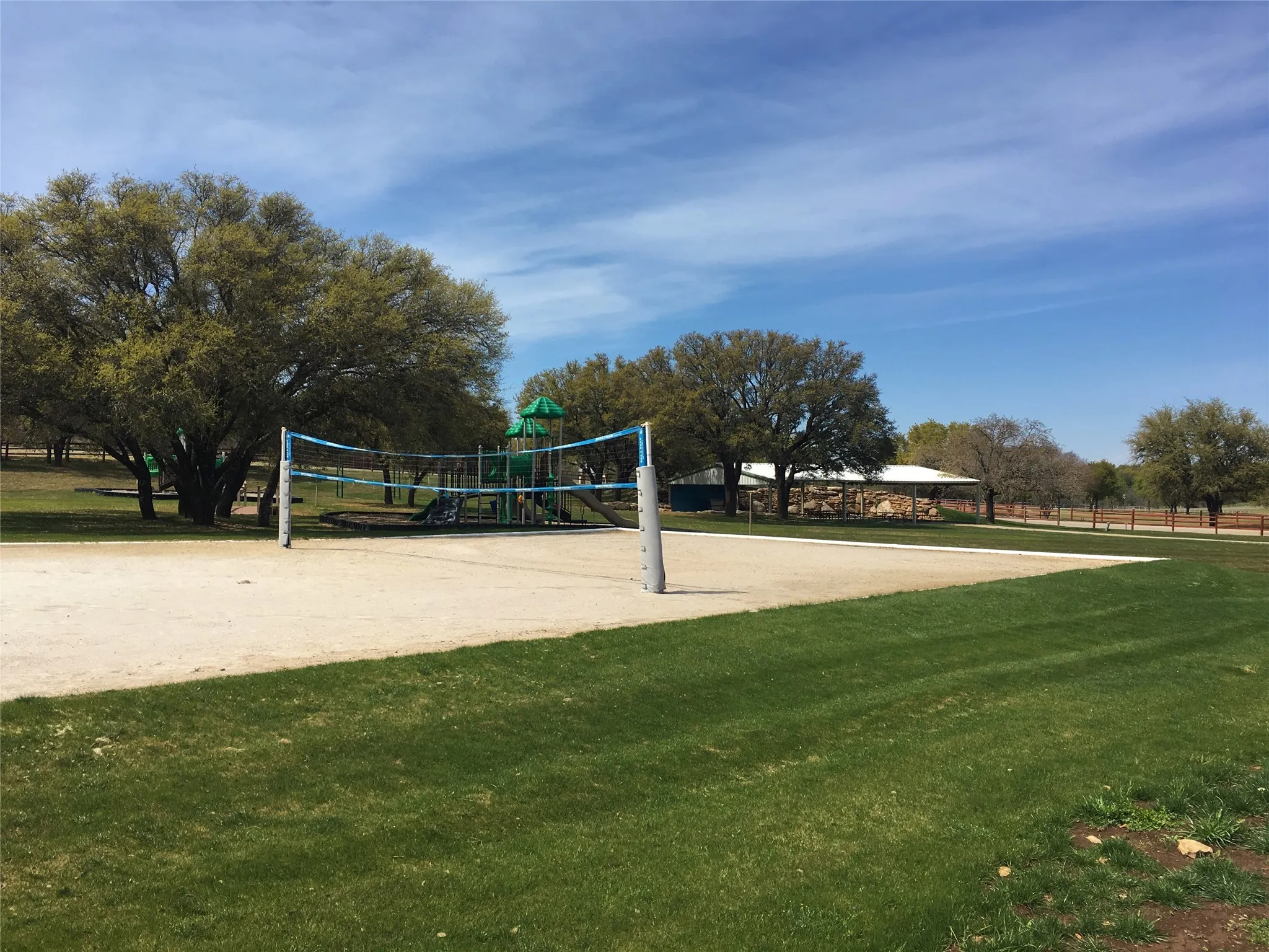 Sand volleyball court with a net, bordered by manicured lawn and mature trees