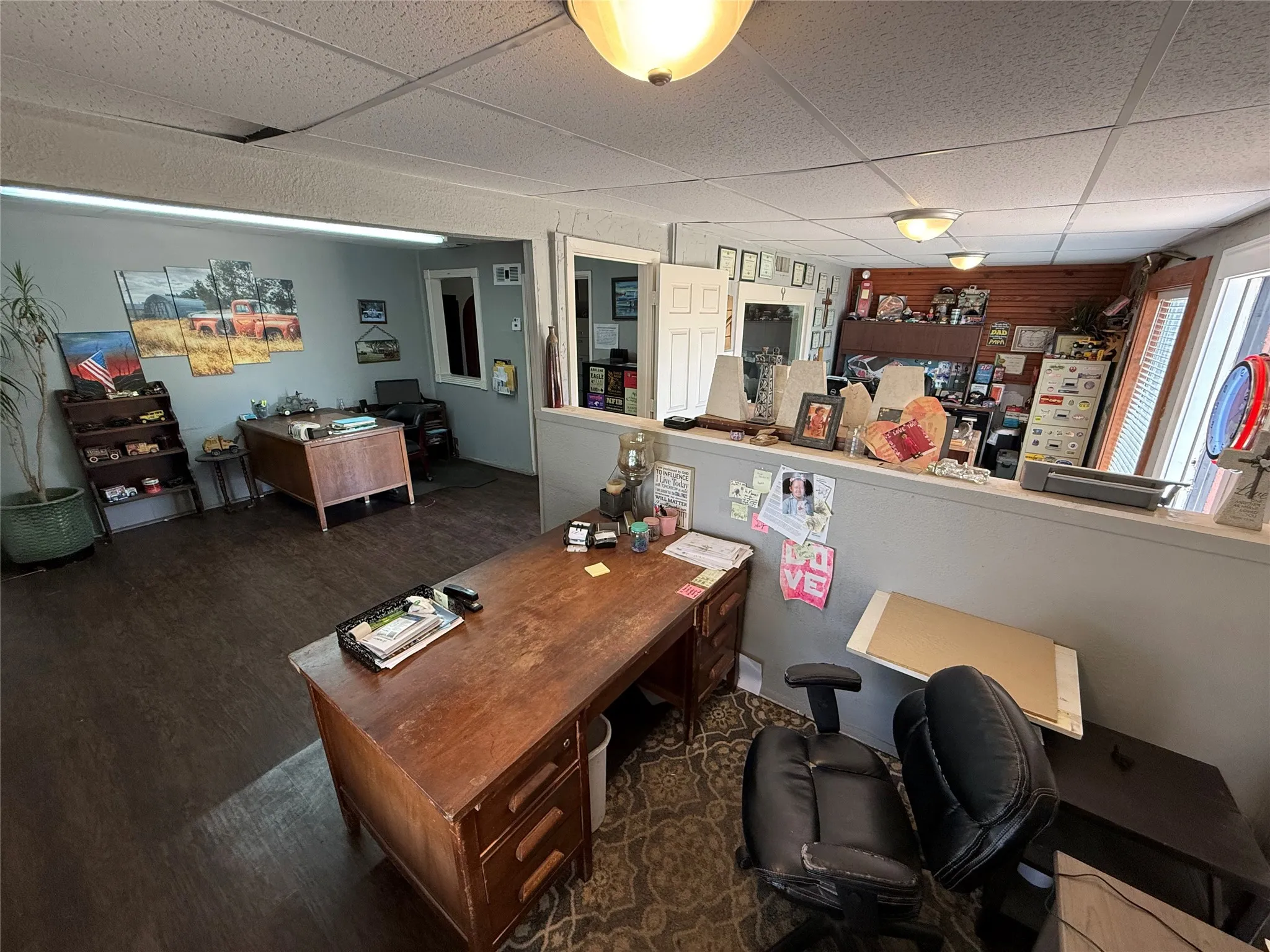 Open-concept office space featuring wood-finish flooring, a drop ceiling with flush-mount lighting, and a partial dividing wall