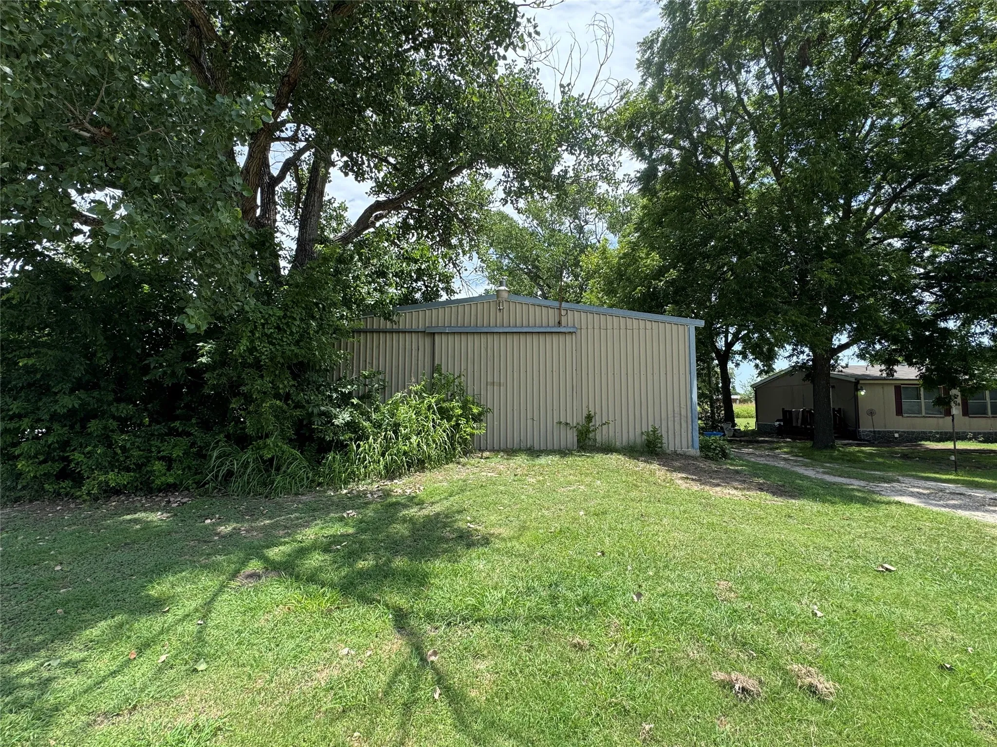 Metal-sided outbuilding with a pitched roof, surrounded by mature trees and established greenery