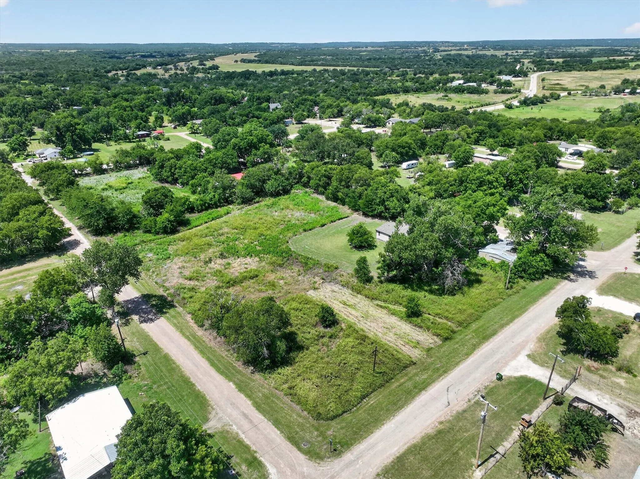 Expansive undeveloped lot with mature trees, surrounded by residential properties and unpaved roads