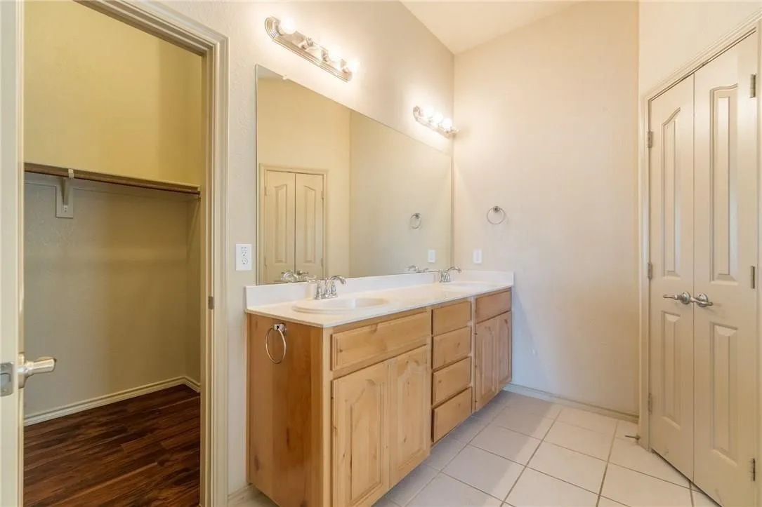 Bathroom featuring a double vanity with wood-finish cabinetry and light-colored countertops, dual sinks with chrome fixtures, and a large wall-mounted mirror