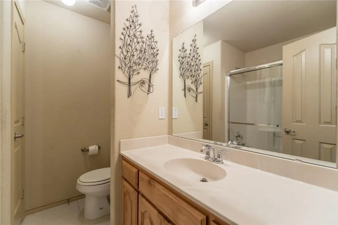 Bathroom vanity featuring a light-toned countertop with integrated sink, chrome faucet, and wood-finish cabinetry