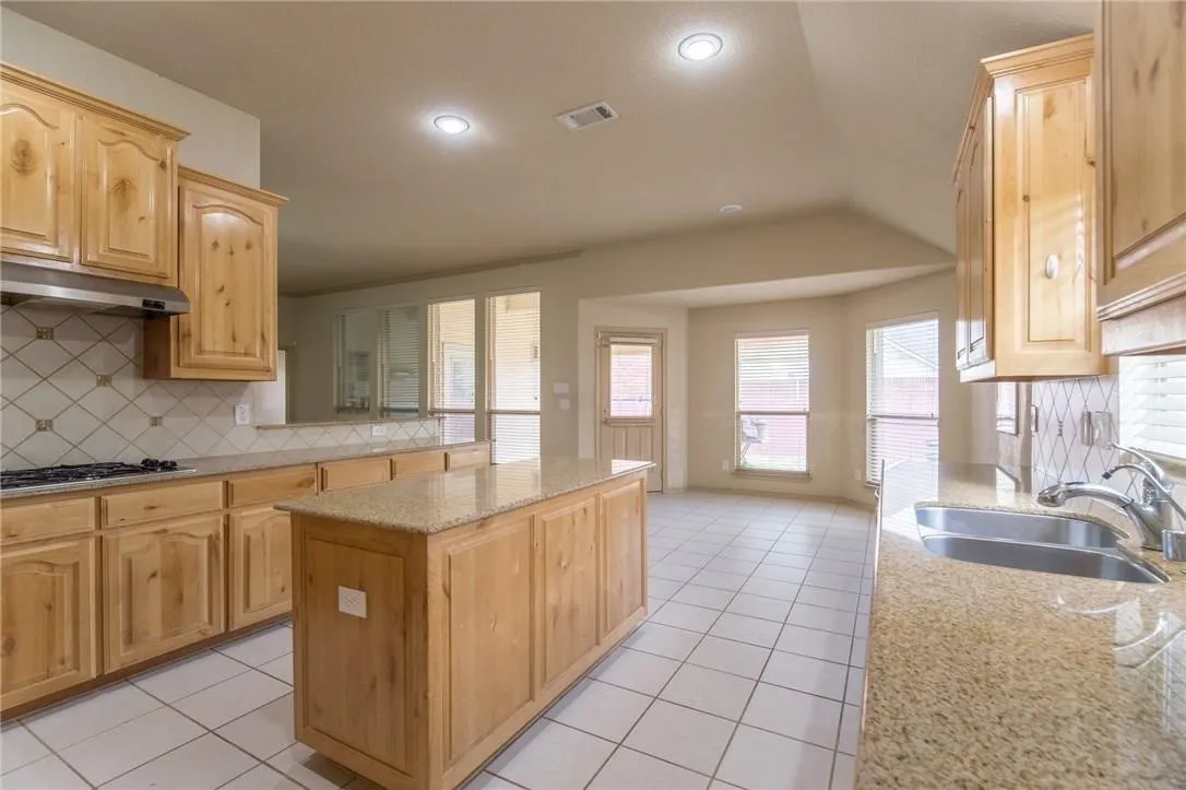Kitchen featuring light wood cabinetry, granite-finish countertops, and a central island