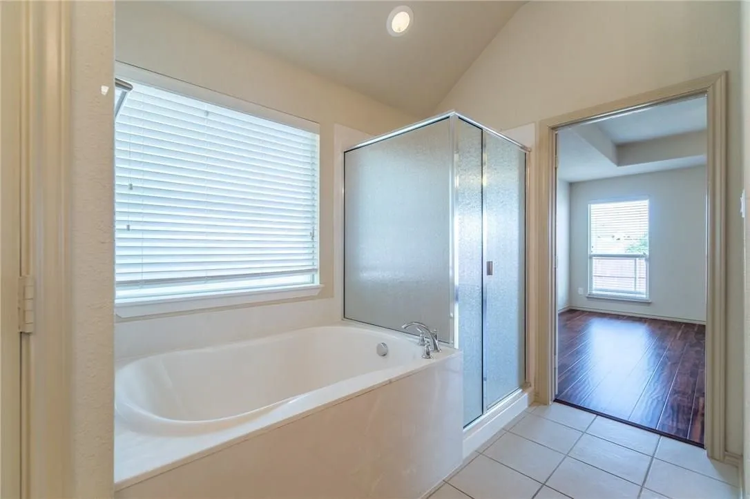 Bathroom featuring a built-in soaking tub, a frosted glass shower enclosure, and white tile flooring