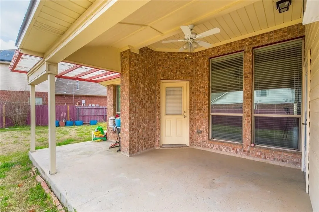 Covered outdoor patio featuring a ceiling fan, brick exterior, and two large windows with blinds