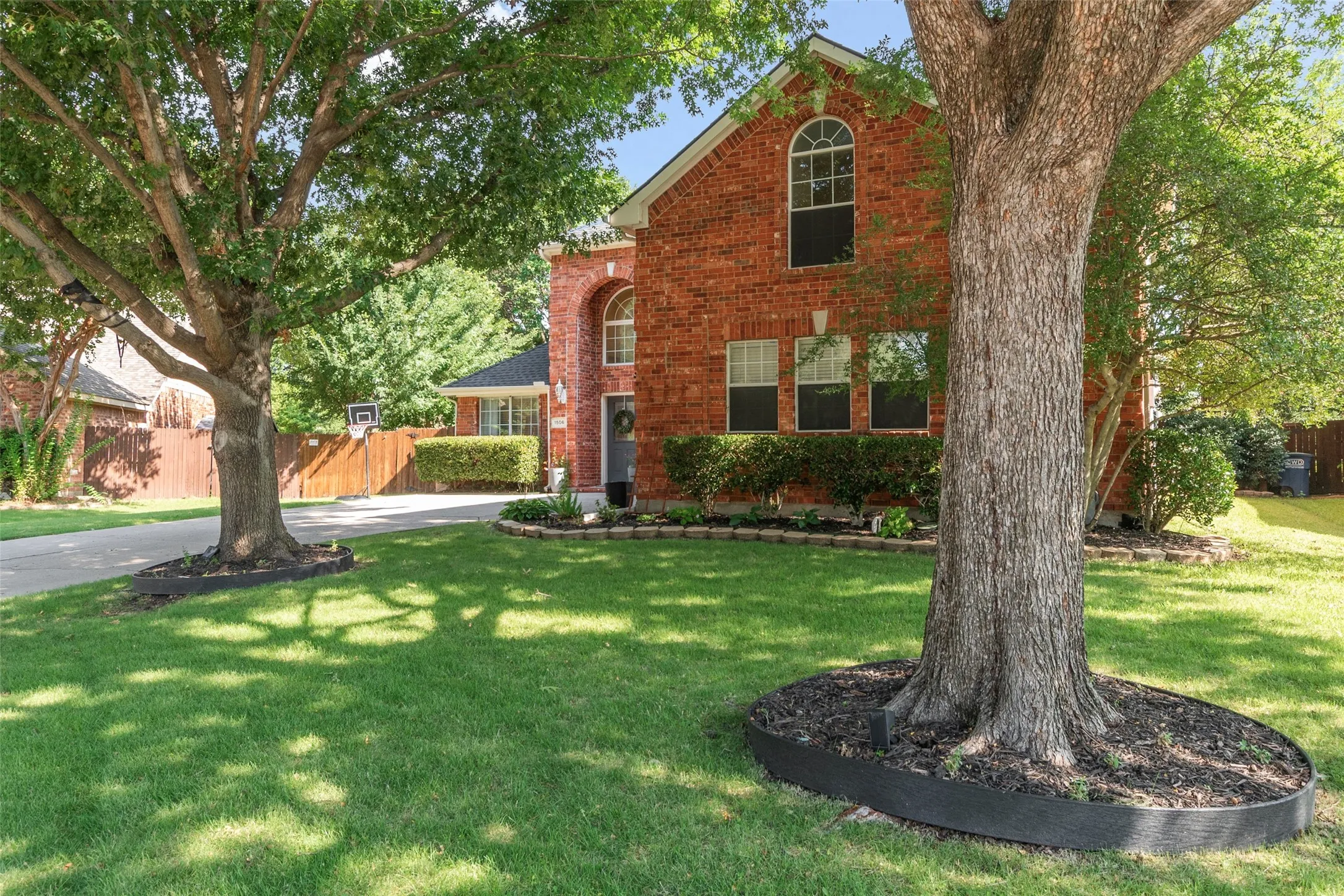 Brick residence featuring an arched window, a prominent front door with sidelights, and a landscaped foundation bed