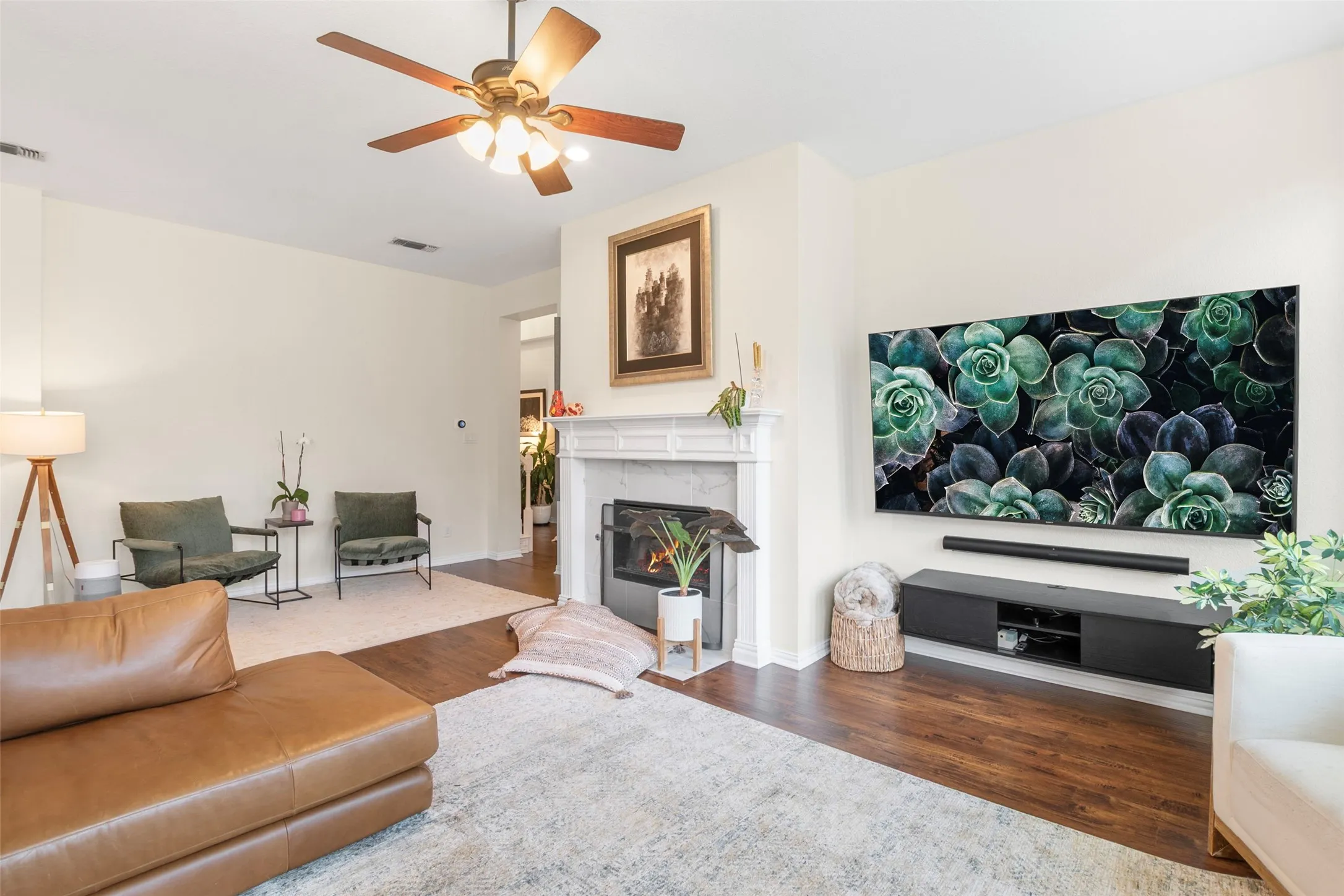 Living area featuring wood-finish flooring, a white mantel fireplace, and a ceiling fan with integrated lighting