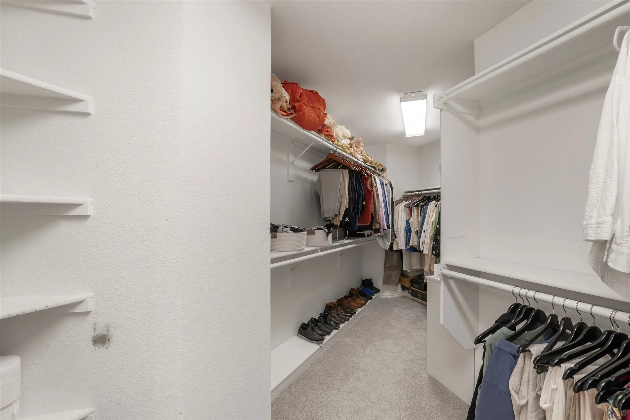 Spacious walk-in closet featuring white wire shelving, hanging rods, recessed ceiling lighting, and light grey carpeting
