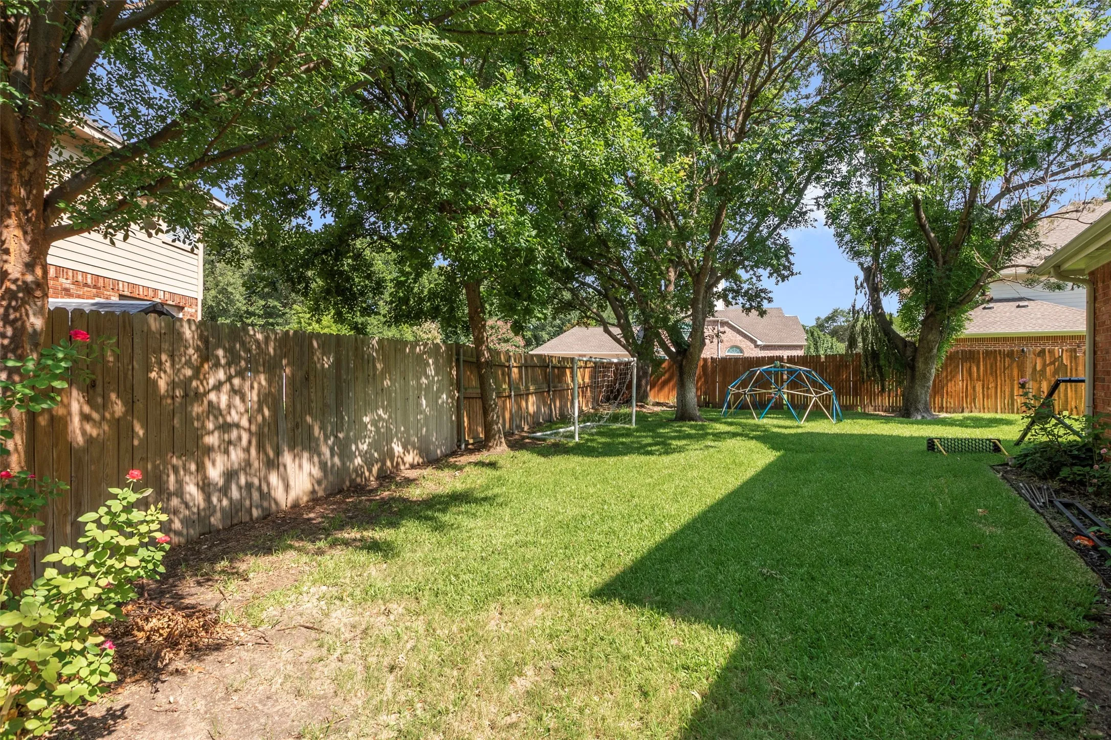 Expansive backyard featuring a lush lawn, mature trees providing shade, and a privacy fence