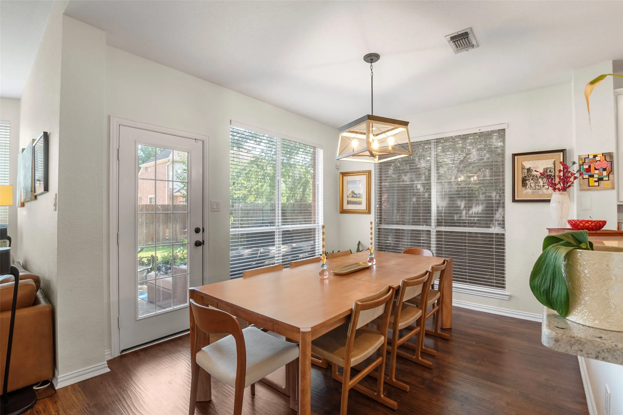 Open-concept dining area featuring wood-finish flooring, a contemporary ceiling fixture, multiple large windows, and a glass-paneled door opening to the exterior