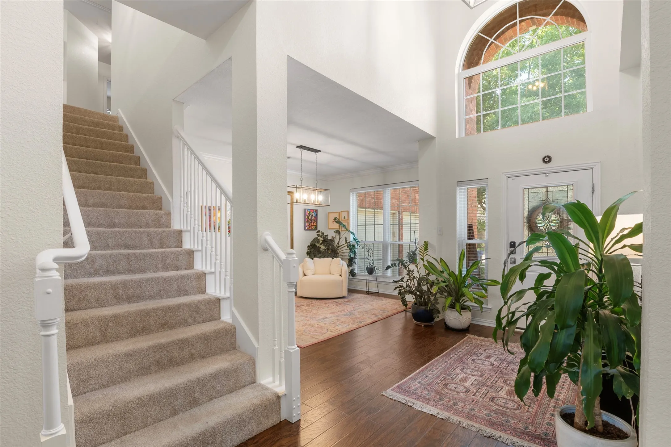 Entryway featuring a two-story ceiling, arched transom window, wood-finish flooring, and a carpeted staircase with white balusters