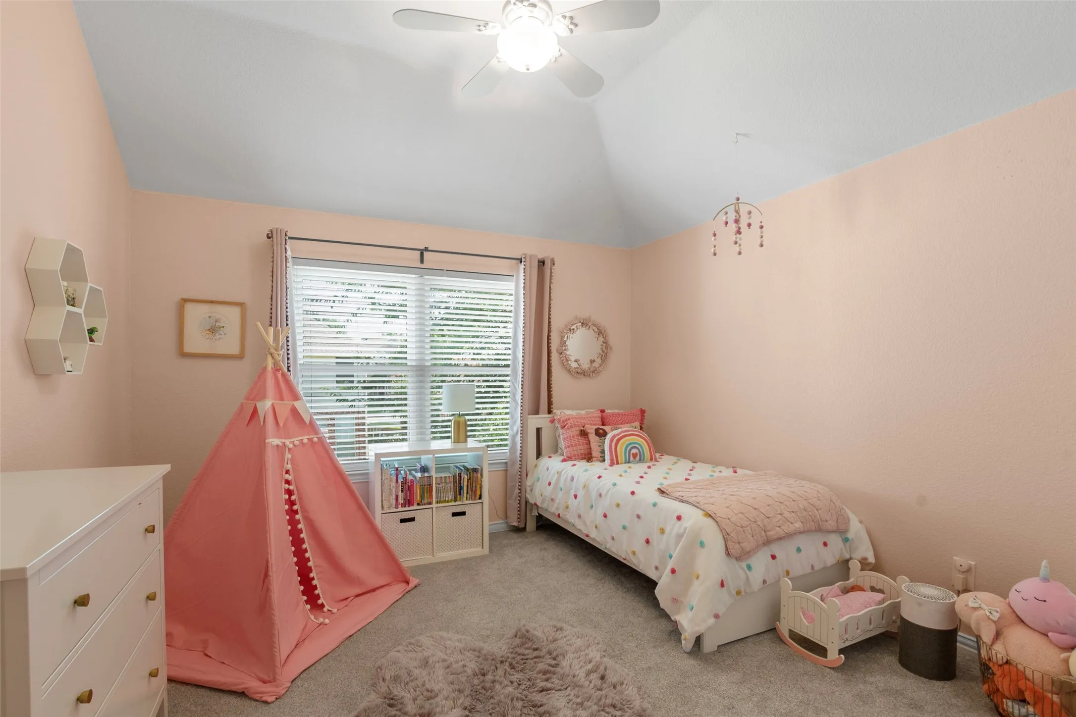 Vaulted ceiling bedroom featuring plush carpet flooring, a ceiling fan with light fixture, and a window with blinds and drapes