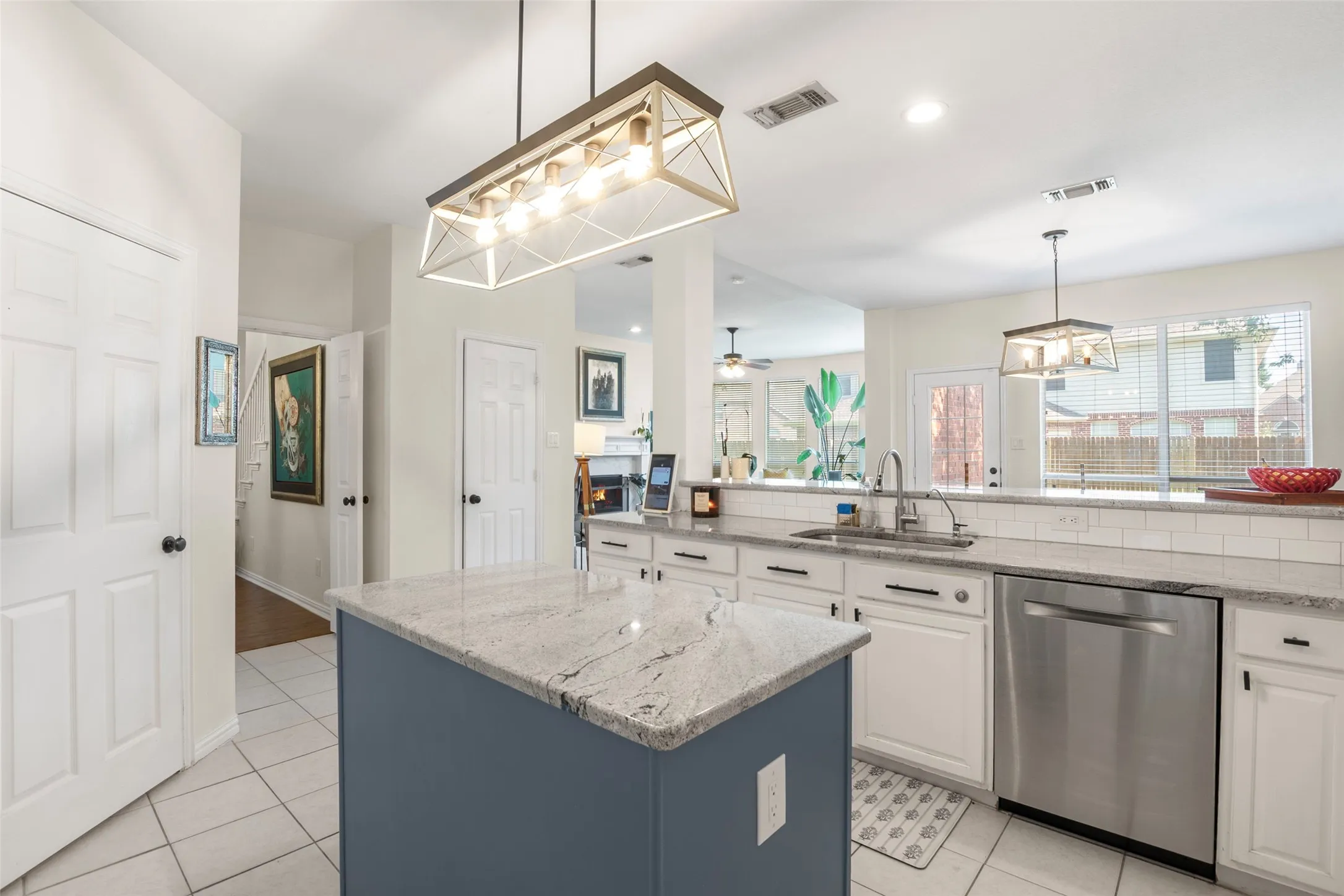 Kitchen featuring a central island with a light-toned countertop, white cabinetry with dark hardware, a stainless steel dishwasher, and a white subway tile backsplash