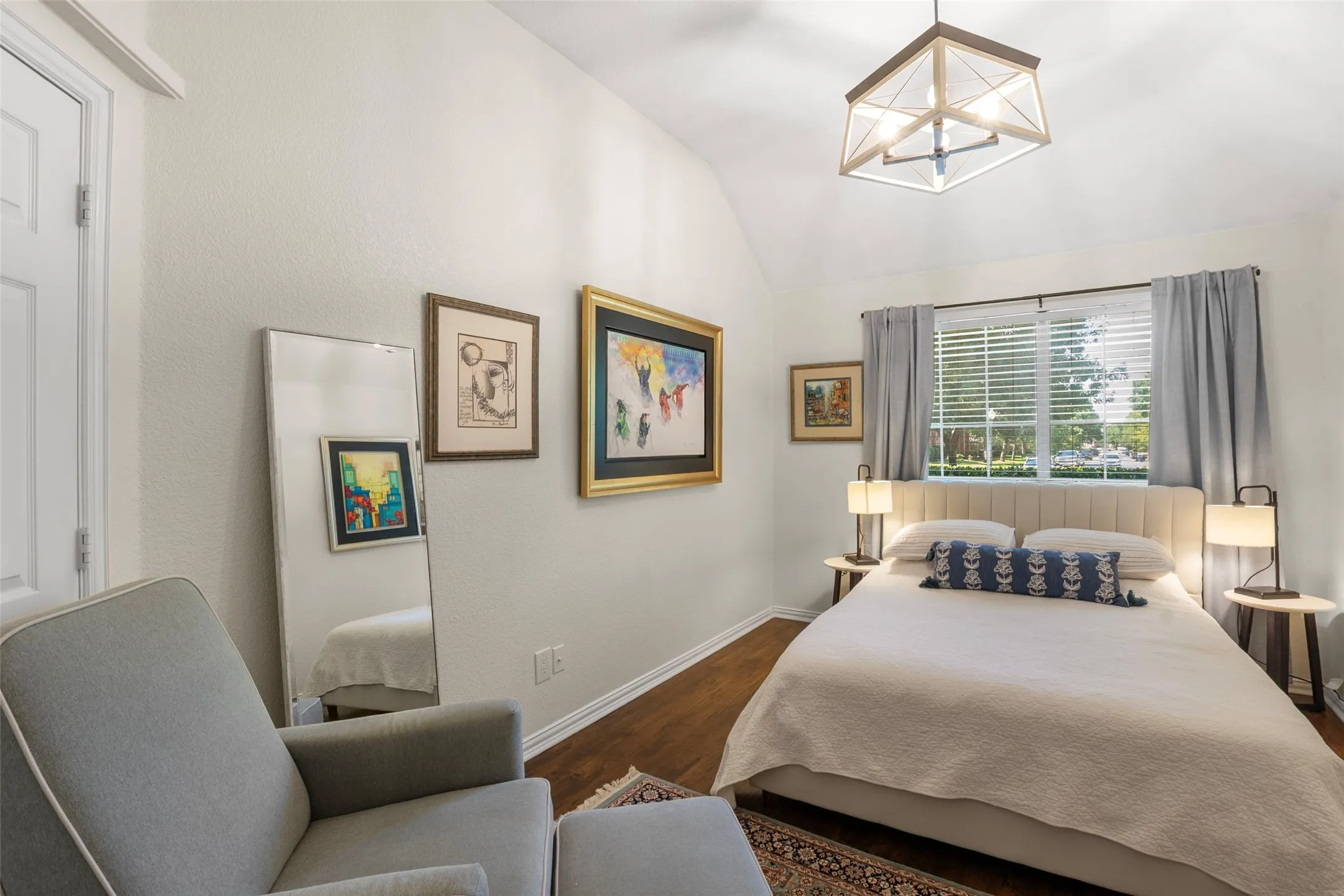 Vaulted ceiling bedroom featuring wood-finish flooring, a window with blinds and drapes, and a contemporary ceiling light fixture