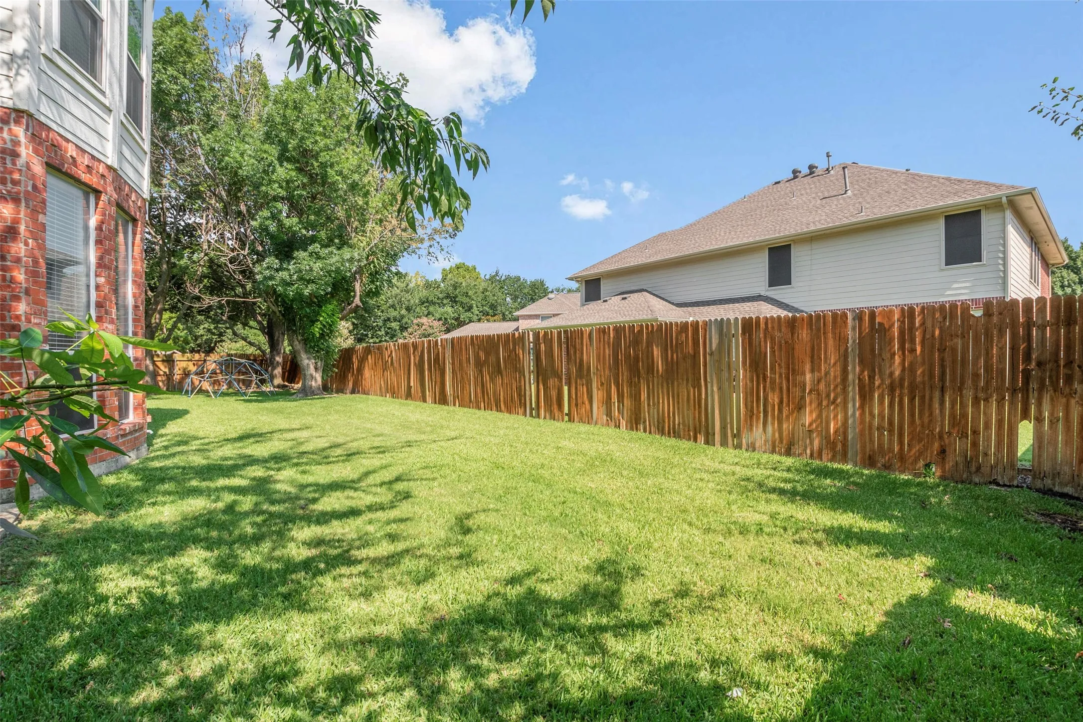 Spacious backyard featuring a manicured lawn, wood privacy fencing, and mature trees