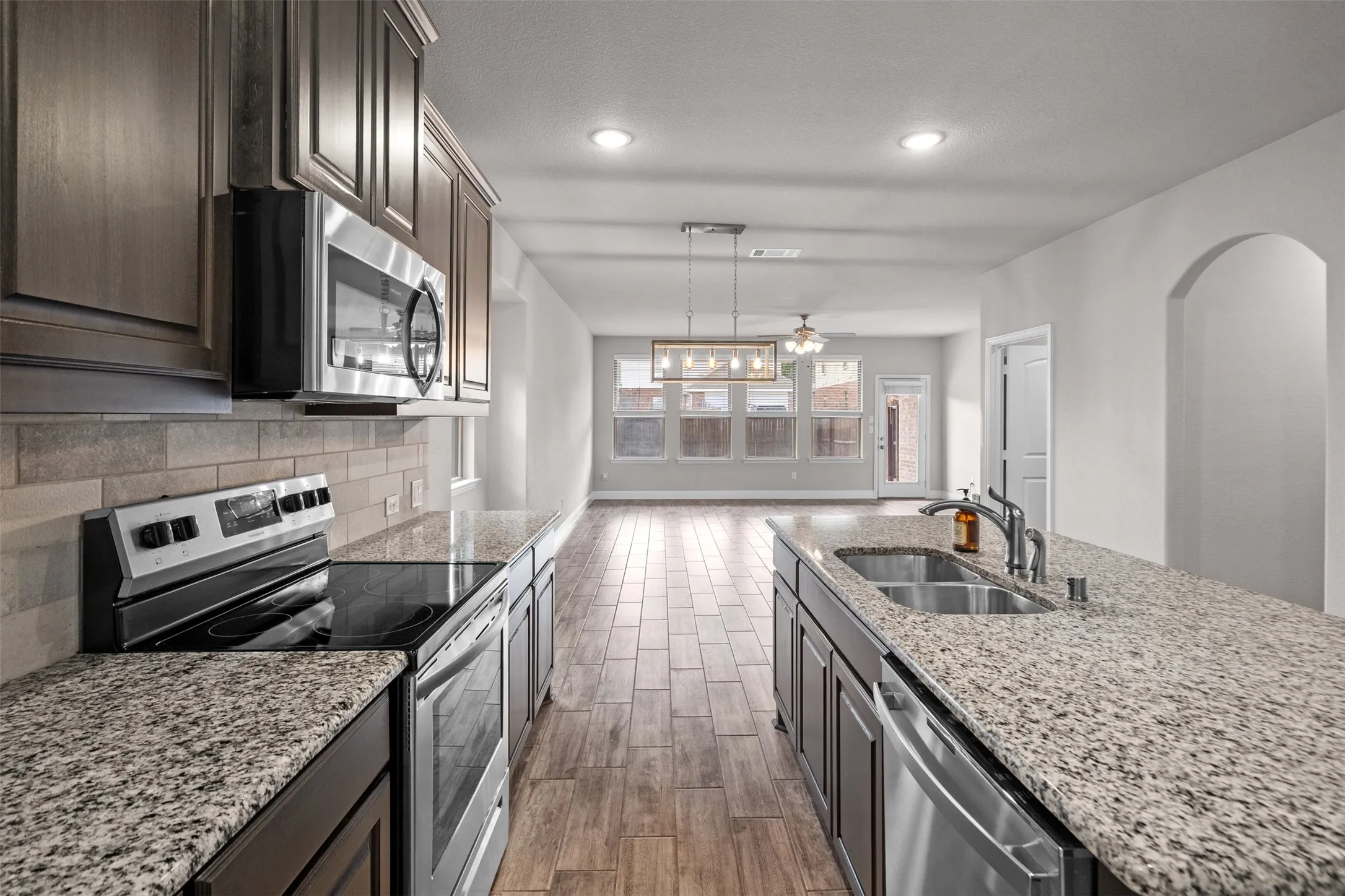 Kitchen featuring granite countertops, stainless steel appliances, dark wood cabinetry, and wood-finish tile flooring