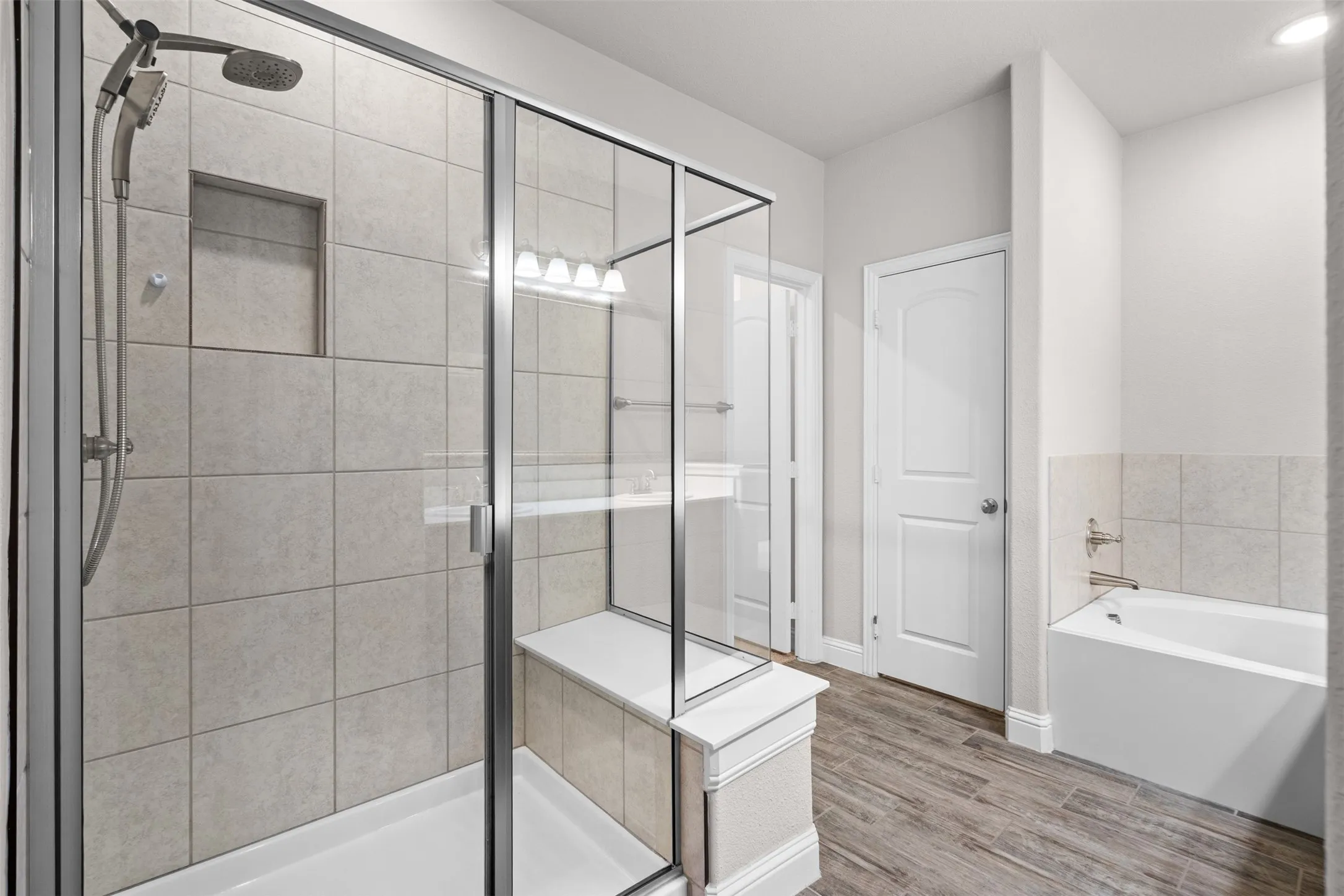 Glass-enclosed shower with a built-in bench and recessed niche, accompanied by a separate soaking tub