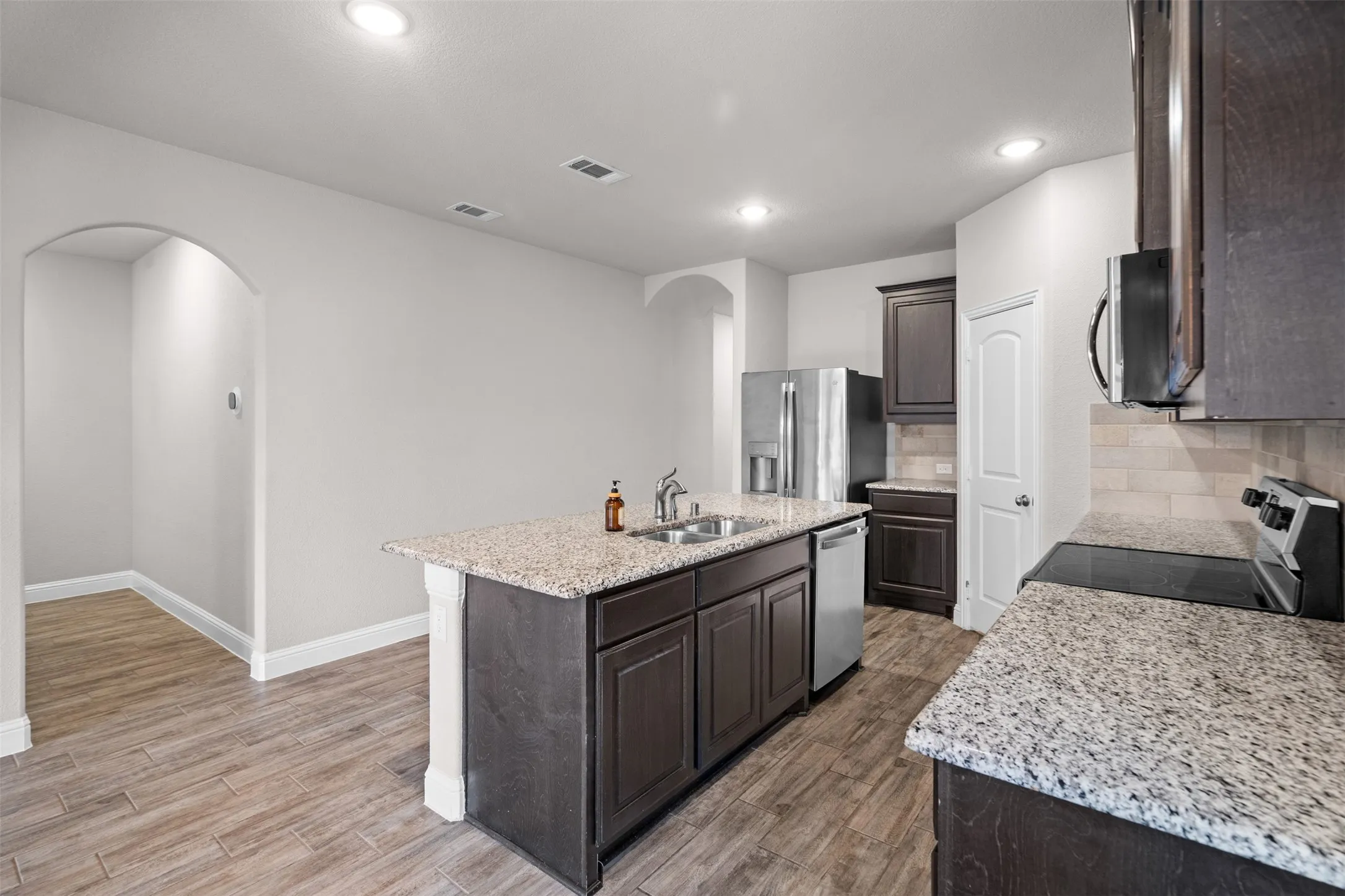 Modern kitchen featuring wood-finish flooring, dark wood cabinetry, and speckled countertops
