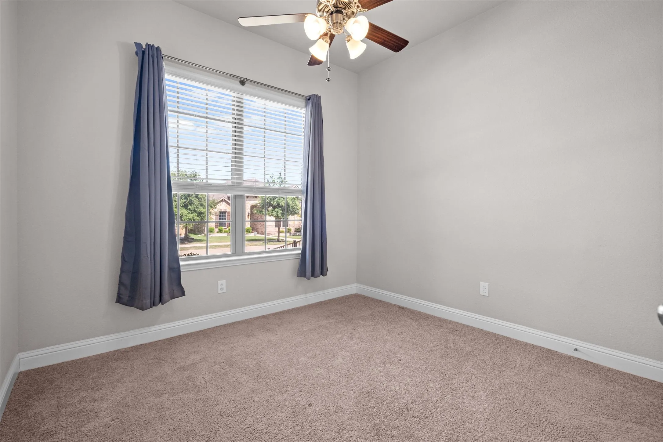 Bright room featuring a large window with blinds and drapes, a ceiling fan with light fixture, light gray wall paint, and neutral-toned carpeting