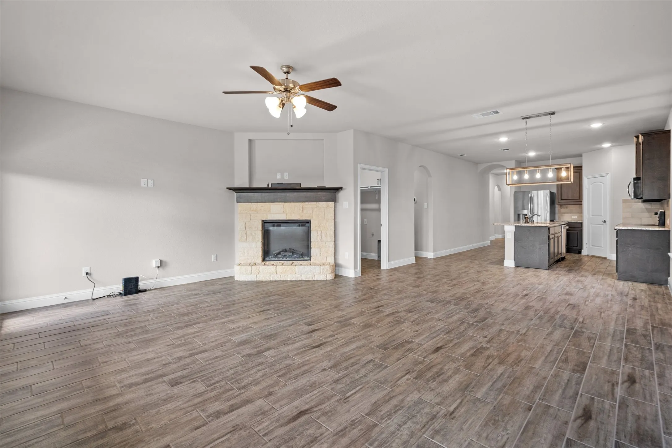 Spacious living area featuring wood-finish tile flooring, a stone-faced fireplace with a dark mantel, and an open concept layout with recessed lighting