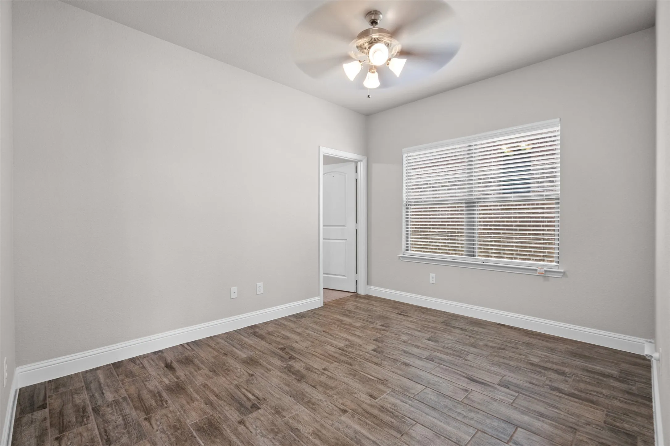 Room featuring wood-finish flooring, light gray walls, white baseboards, and a window with horizontal blinds
